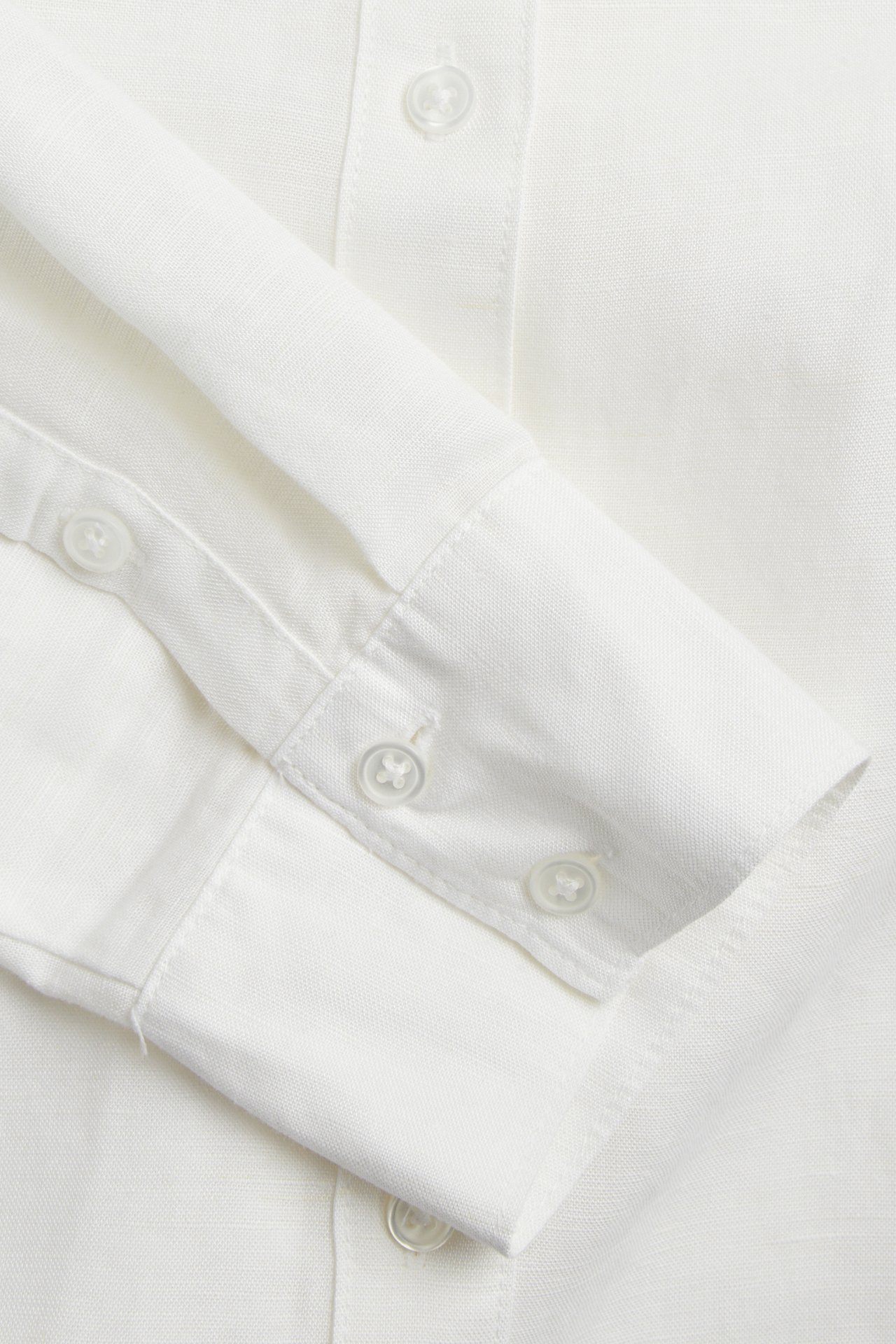 Närbild av en vit linneblandningsskjorta, som visar knappar på knappslån och manschetten.