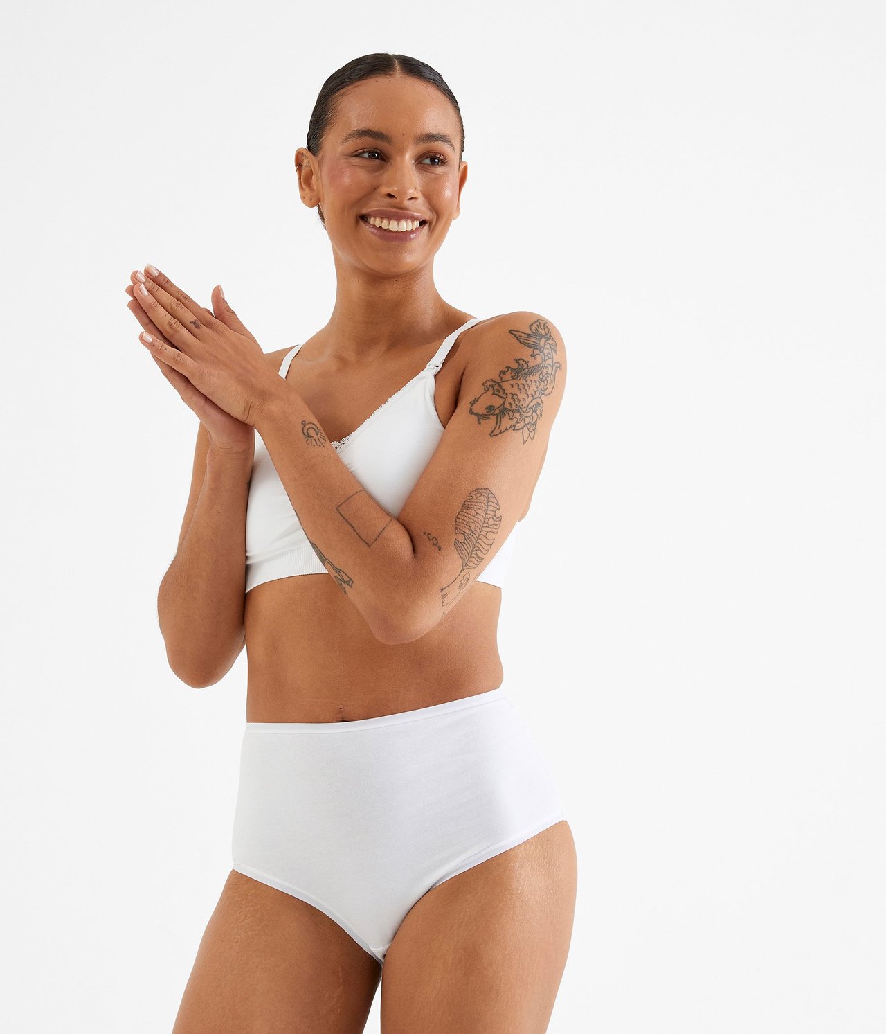 Widok z przodu uśmiechniętej kobiety w białych, wysokich majtkach bawełnianych i białym biustonoszu.