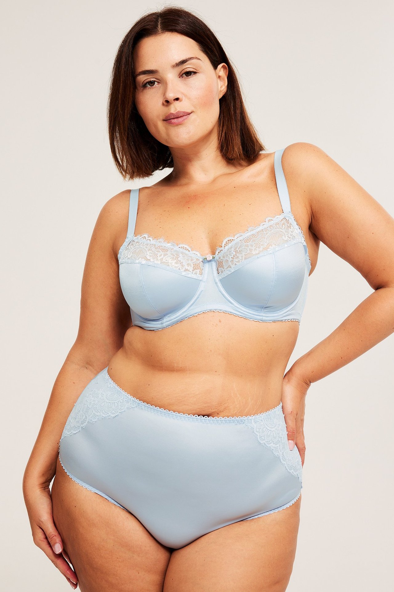 Forfra, kvinne i lyseblå sateng-BH med spile og blondekant samt matchende høy midje truse.