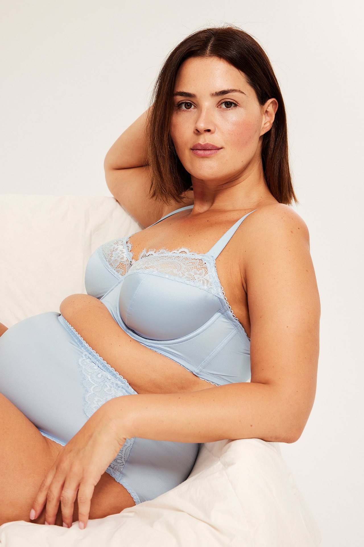 Nærbilde av gravid kvinne i lyseblå spile-BH i sateng med blonder og matchende truse.