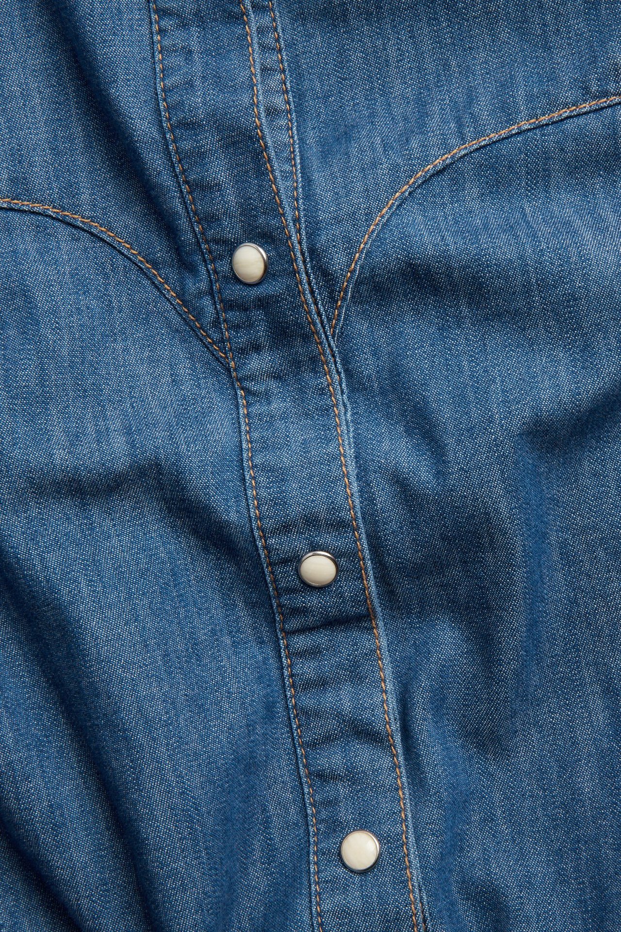 Lähikuva edestä sinisestä farkkupaidasta, jossa on western-kaarroke ja luonnonvalkoiset painonapit.