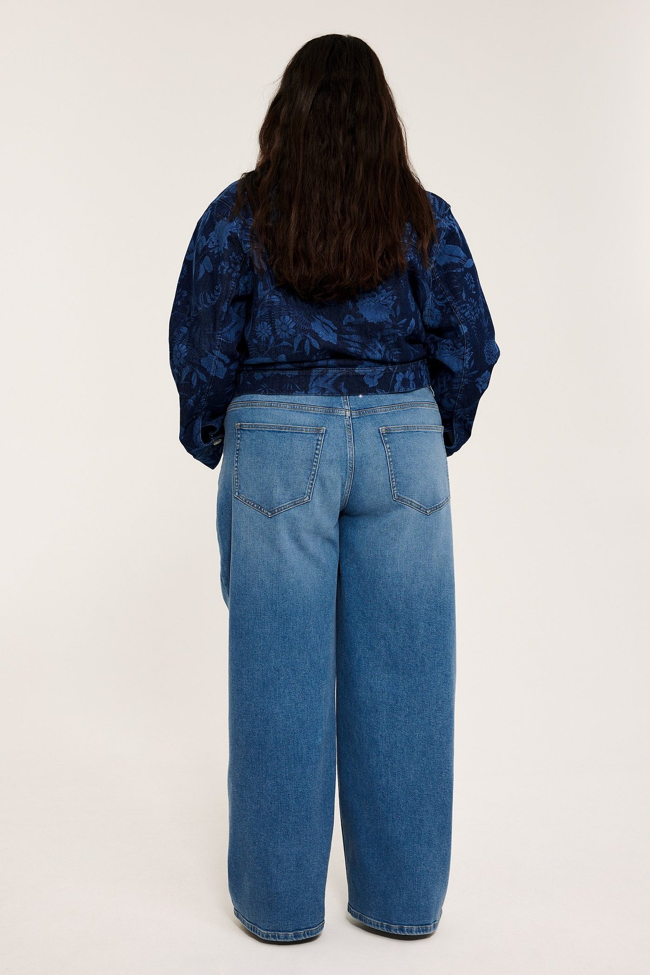 Kvinnas rygg, i ljusblå denim höga raka vida jeans och en mörkblå mönstrad topp.
