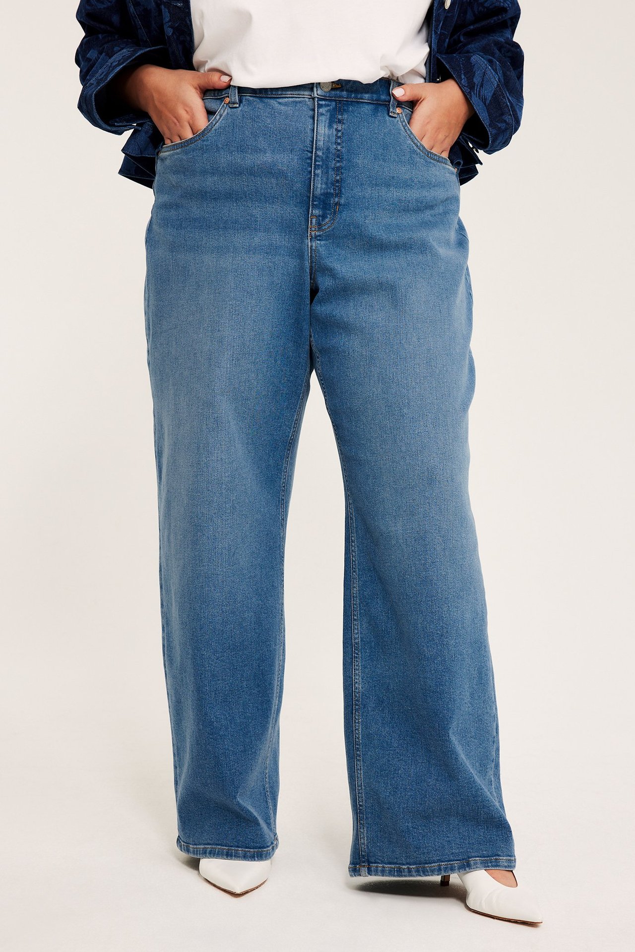 Etunäkymä: Nainen yllään vaaleansiniset korkeavyötäröiset suorat farkut, valkoinen t-paita ja valkoiset avokkaat.