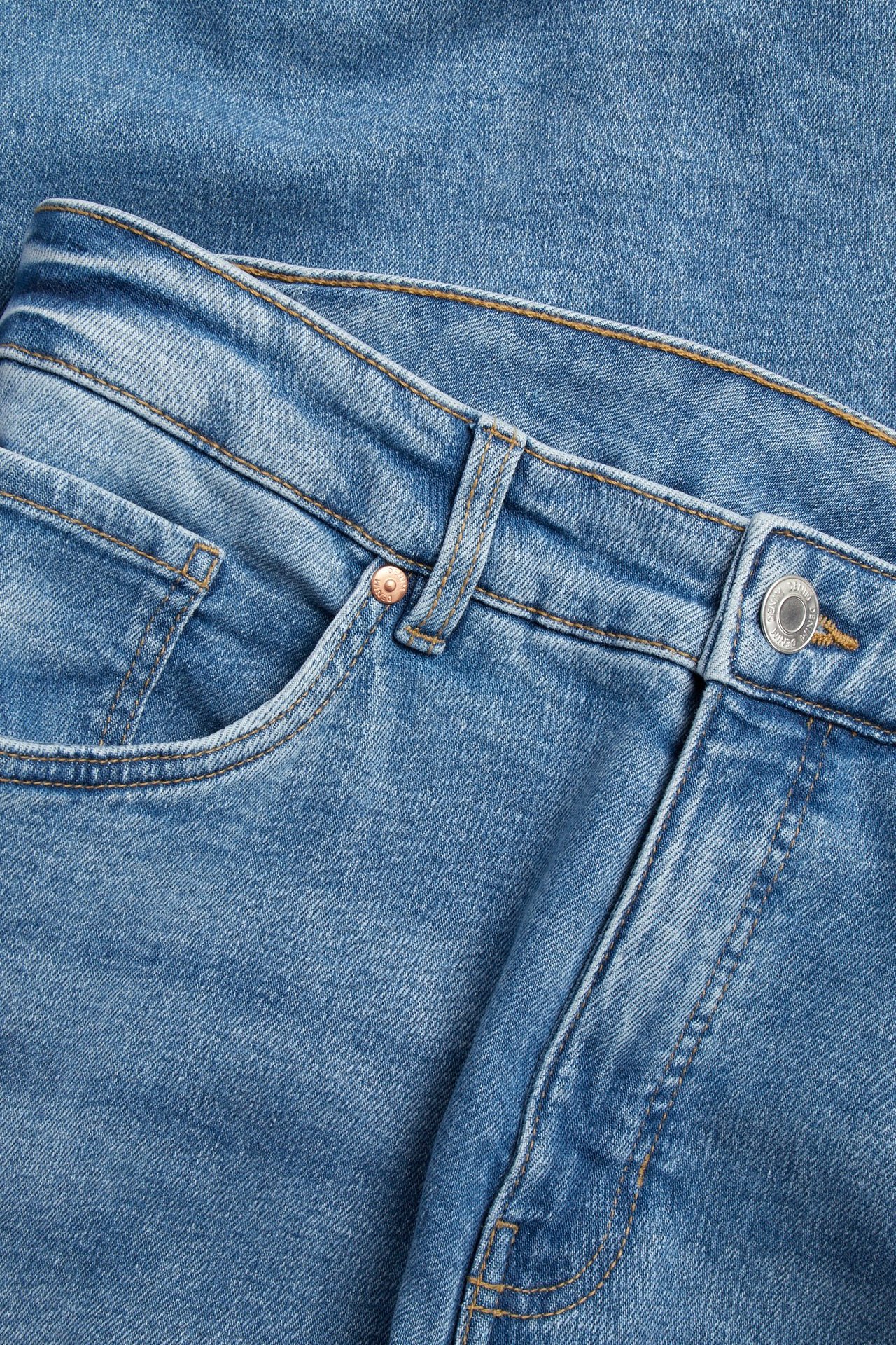 Närbild av ljusblå raka jeans med hög midja, framficka, nit och knappstängning.