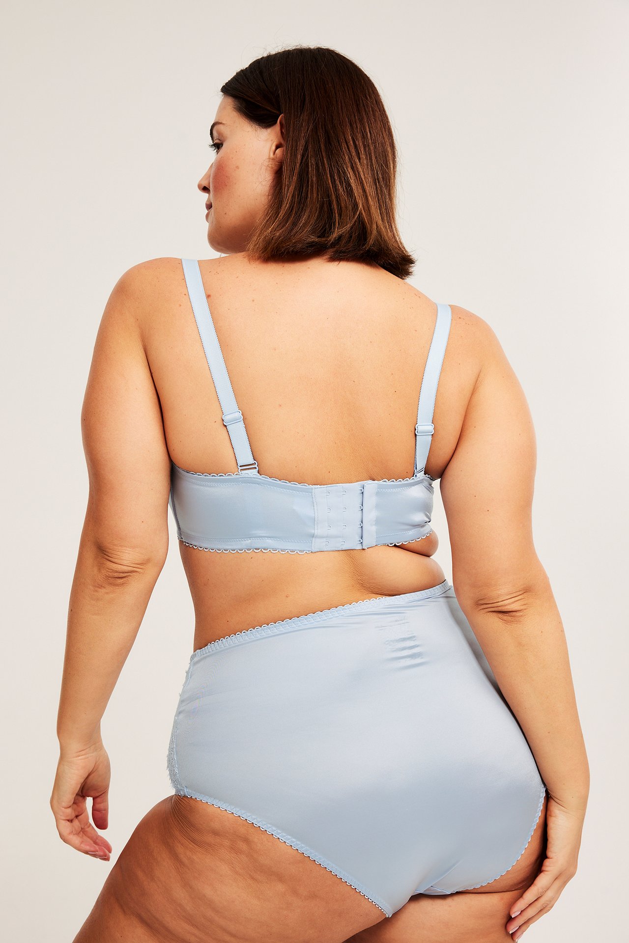 Takakuva naisesta yllään vaaleansiniset pitsireunaiset alushousut ja yhteensopivat rintaliivit.