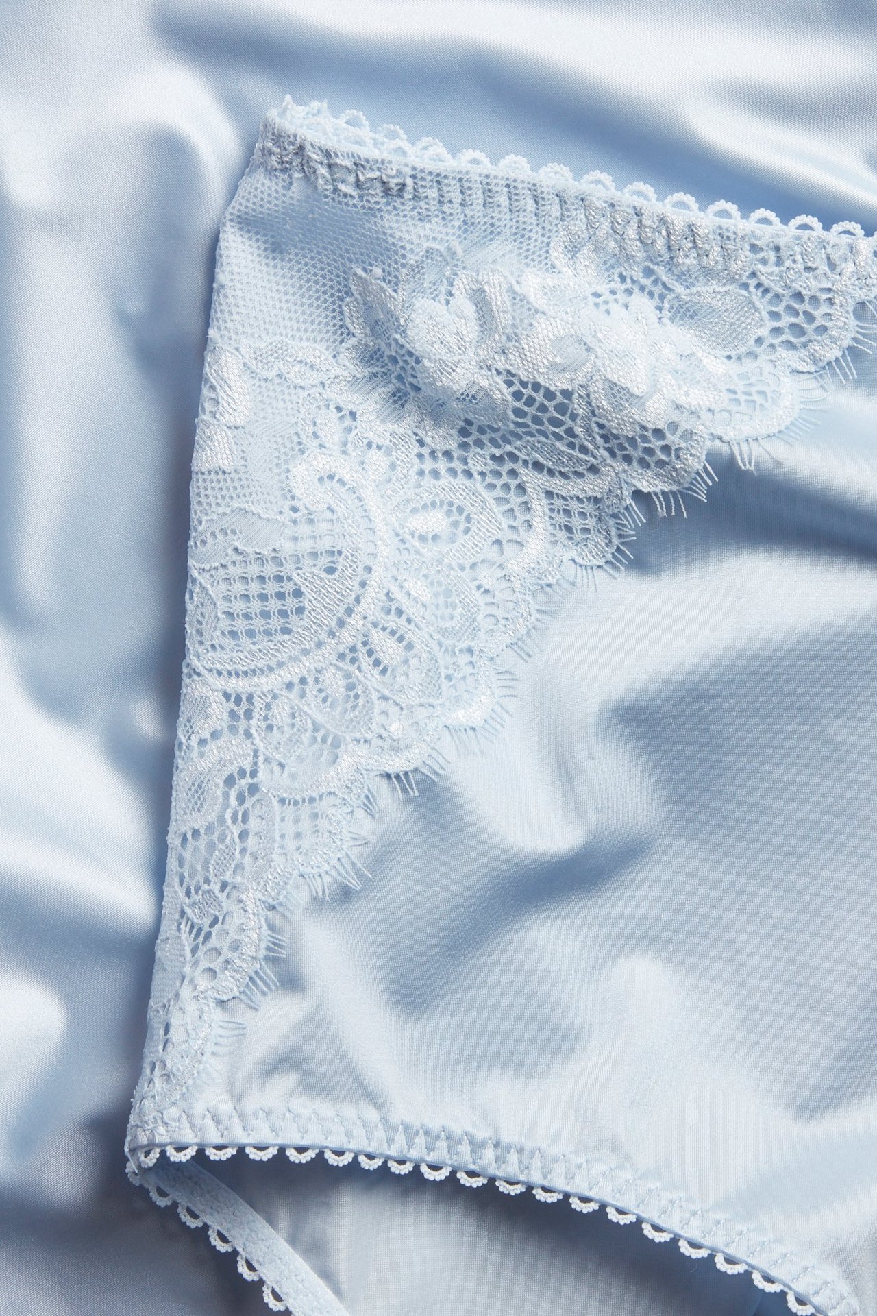 Lähikuva vaaleansinisistä alushousuista, joissa herkkä pitsireuna ja aallotettu reuna.
