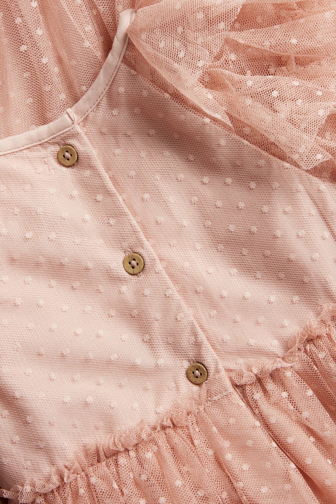 Zbliżenie na różową sukienkę dziecięcą z siateczki w białe kropki, z drewnianymi guzikami i falbankami.