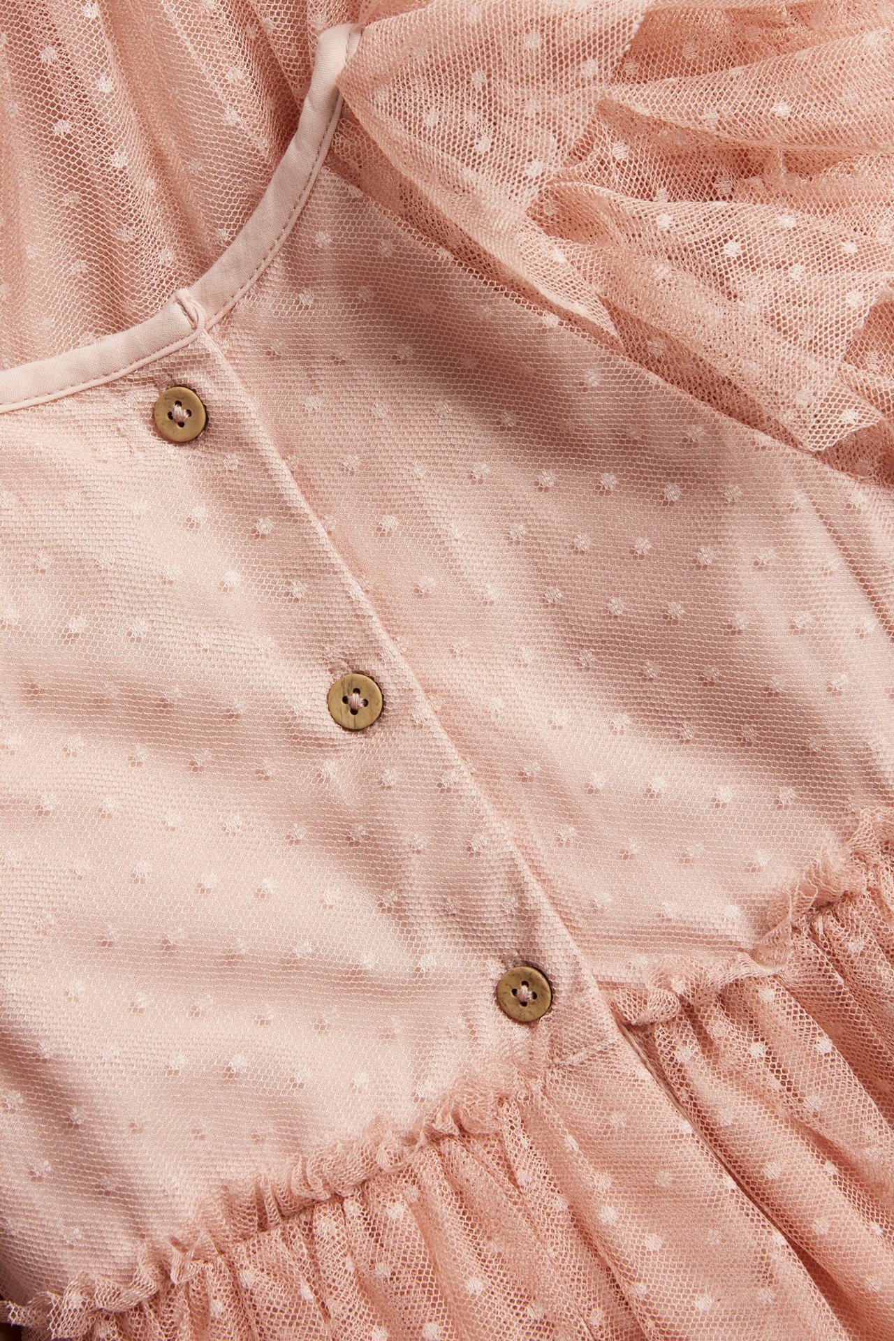 Nærbilde av en rosa prikkete meshkjole til barn med treknapper og volanger.