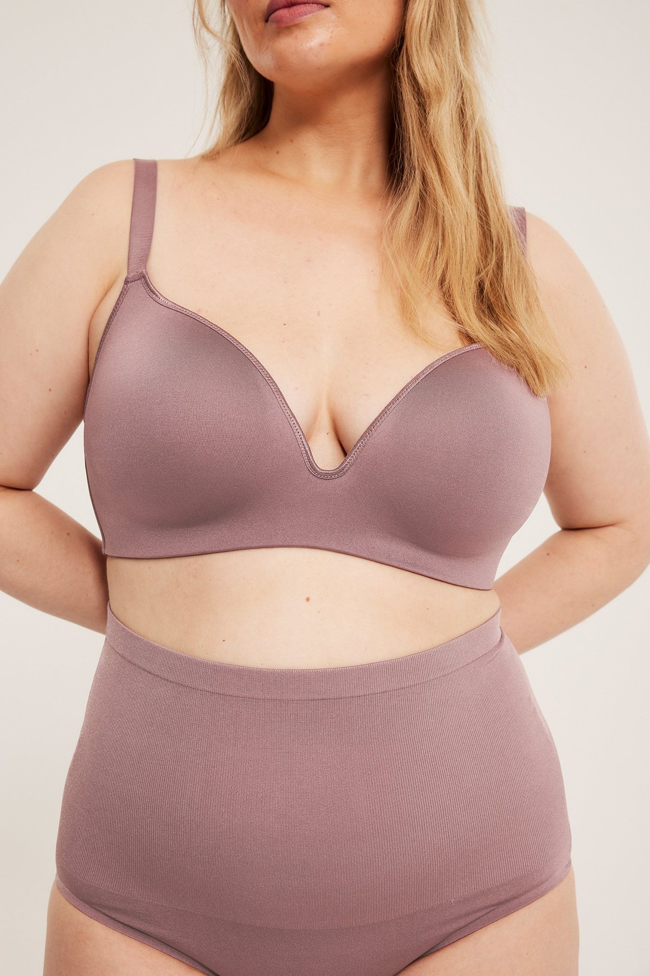 Z przodu, kobieta w bezszwowym, ciemnoróżowym biustonoszu z gładkimi miseczkami i pasujących majtkach z wysokim stanem.
