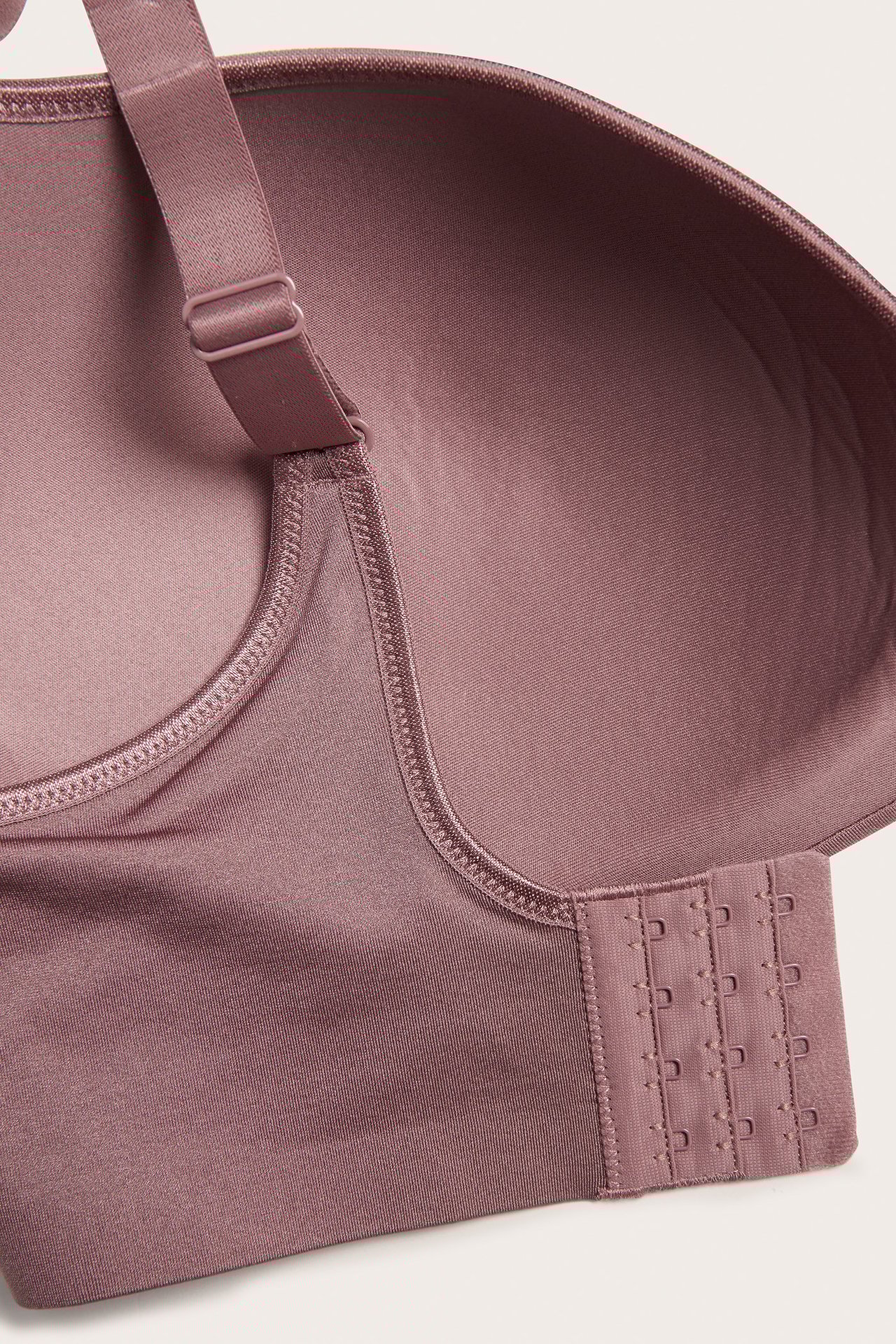 Närbild av mörkrosa sömlös bh: slätt tyg, justerbar rem, trippel hak- och hyskknäppning.