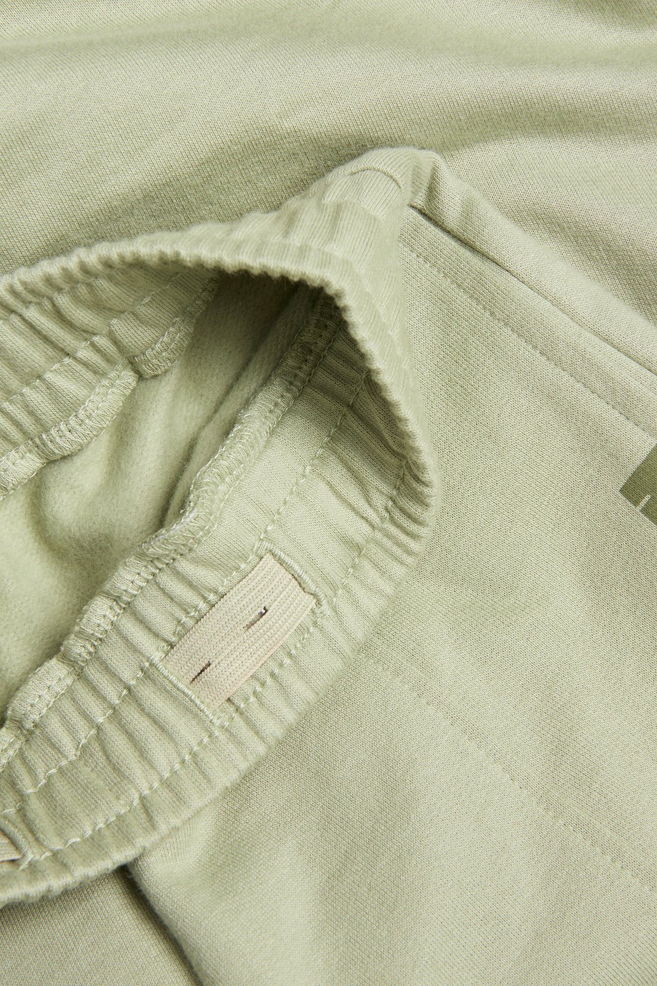 Zbliżenie na jasnozielone bawełniane dresy dla dzieci z elastyczną talią i regulowaną wewnętrzną gumką.