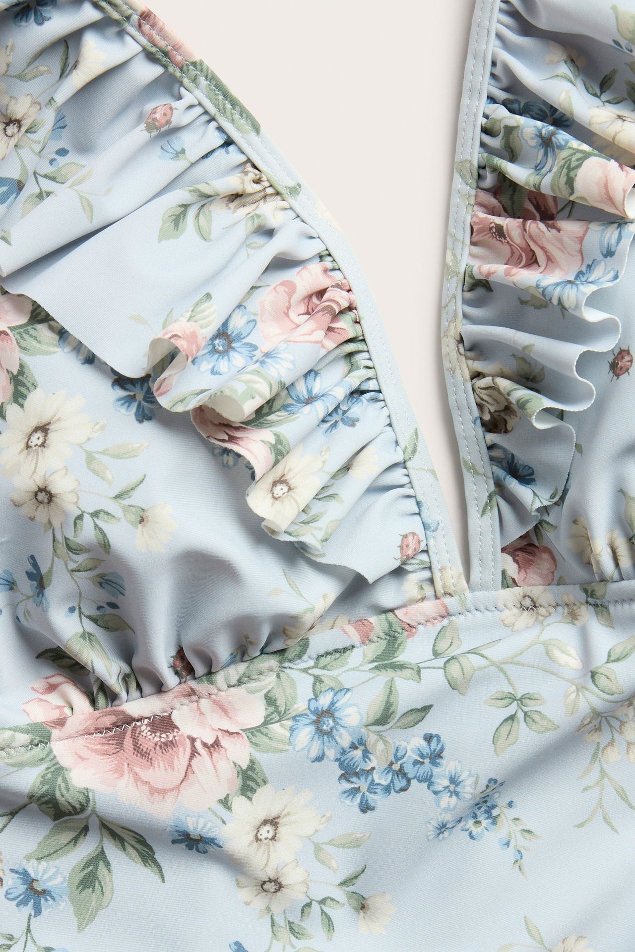 Zbliżenie na jasnoniebieski kwiecisty kostium kąpielowy z falbanami wzdłuż dekoltu w serek.