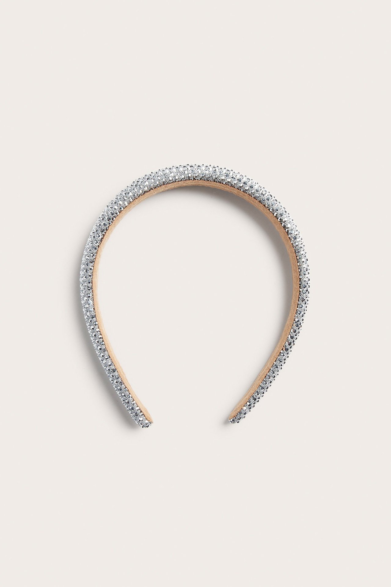Framsida av ett silverfärgat diadem, helt täckt med strass på ett beigt polyesterband.