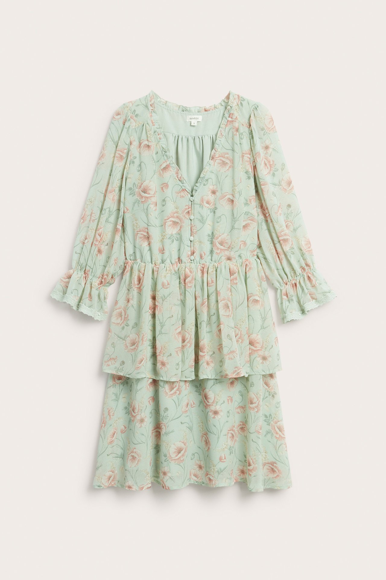 Forfra, lysegrønn blomstret chiffonkjole med volanger, V-hals og stofftrukne knapper.