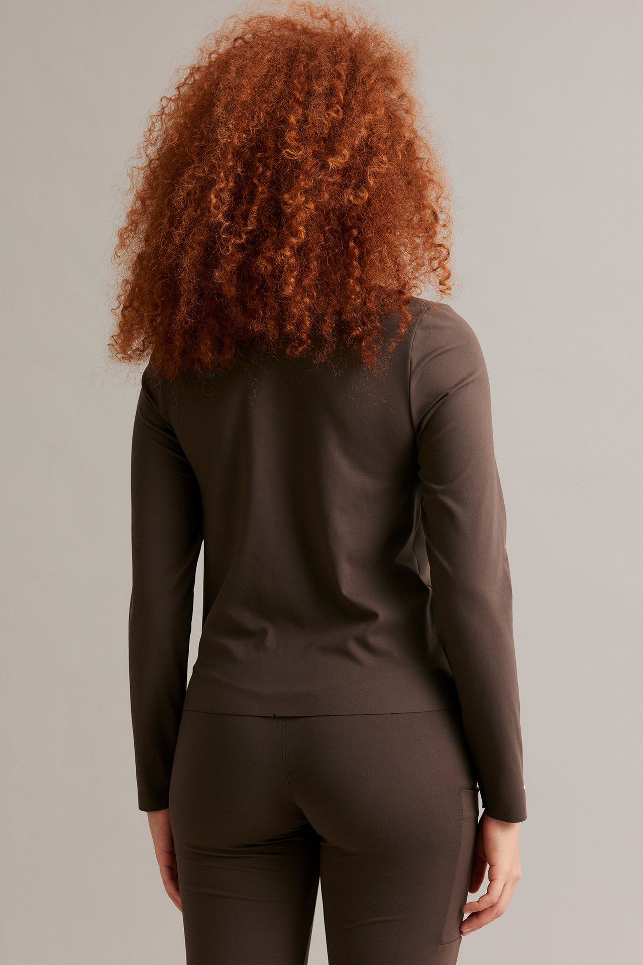 Naisen takaa otettu kuva, yllään yksivärinen ruskea pitkähihainen treenitoppi ja tyköistuvat treenihousut.