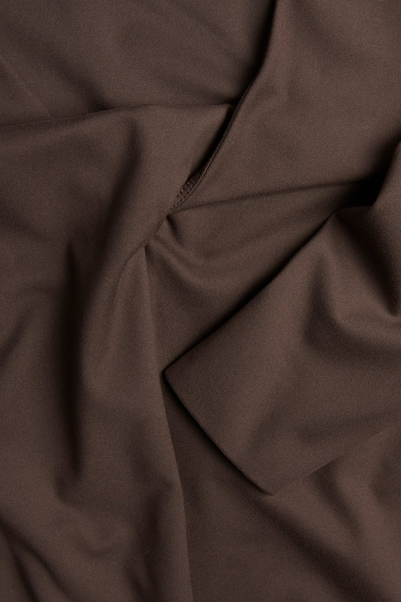 Zbliżenie na brązowy, jednolity top treningowy z dzianiny z dekoltem V typu kopertowego.