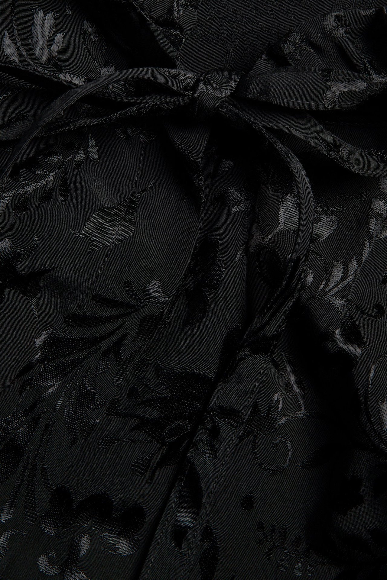 Zbliżenie czarnej żakardowej bluzki z delikatnym wzorem kwiatowym i wiązaną tasiemką na kokardę.