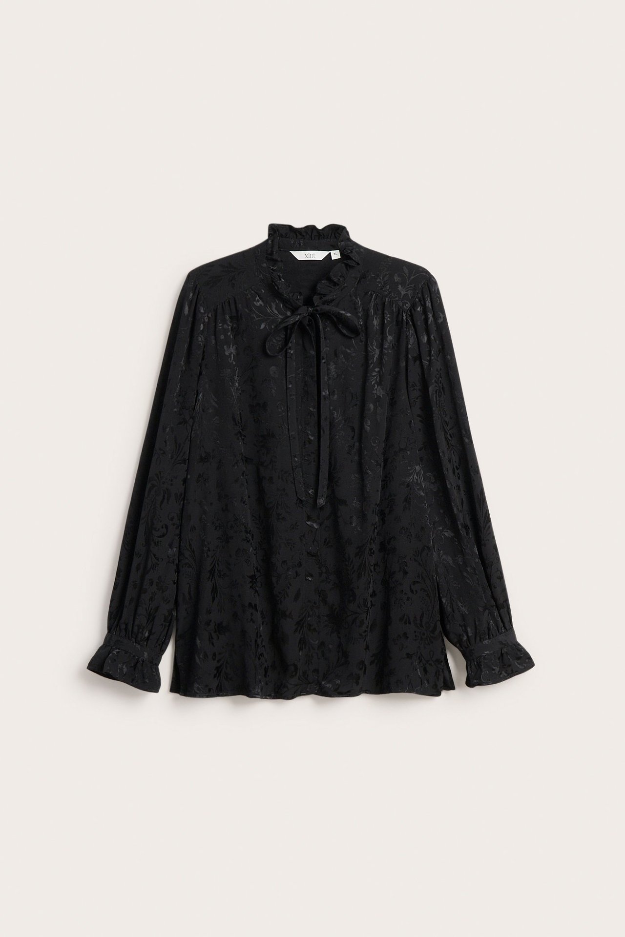 Z przodu czarna żakardowa bluzka wiskozowa z falbanami, wiązaniem i długimi rękawami.