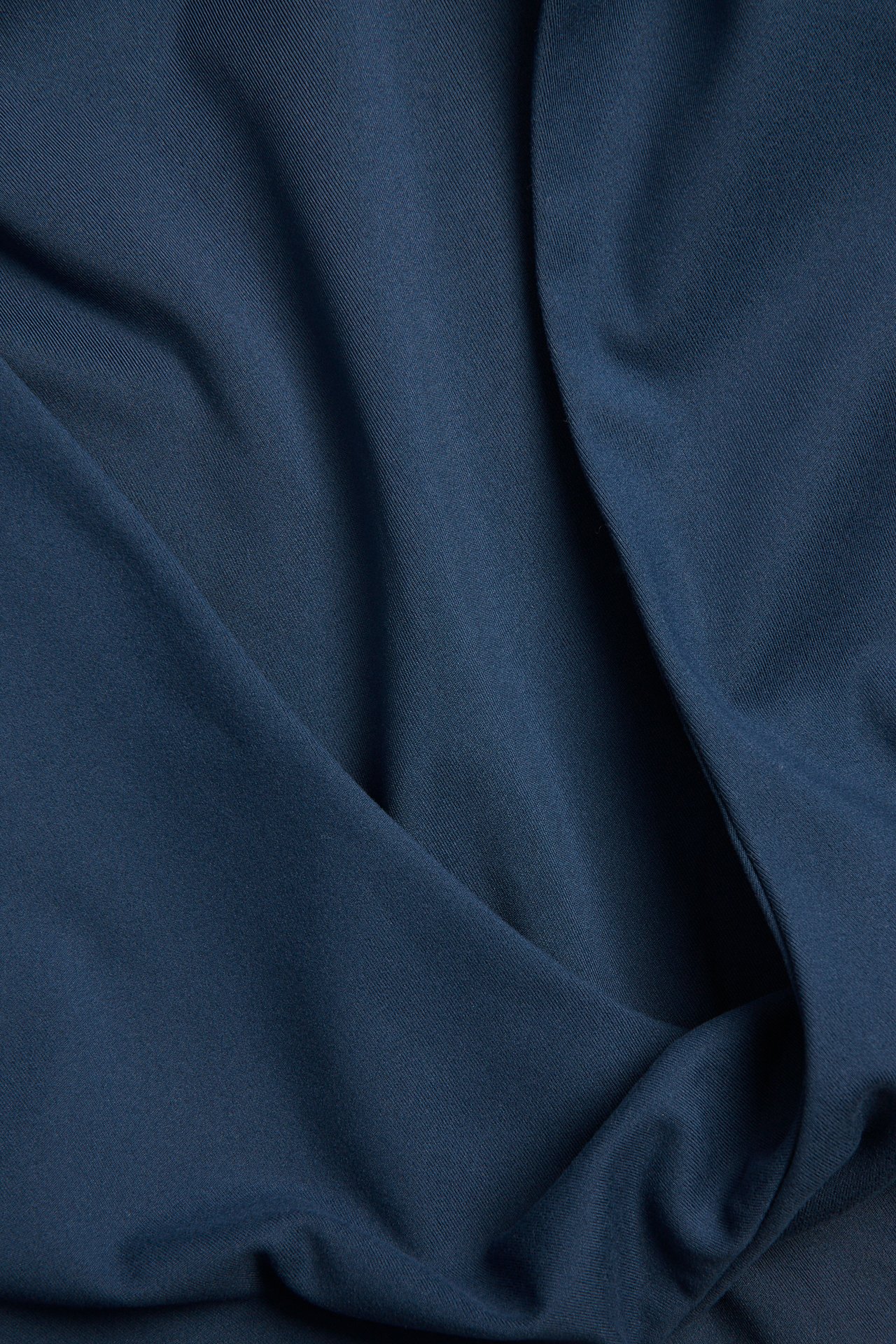 Närbild på toppens mjuka, matta blåa stretchjerseytyg, med milda draperingar.