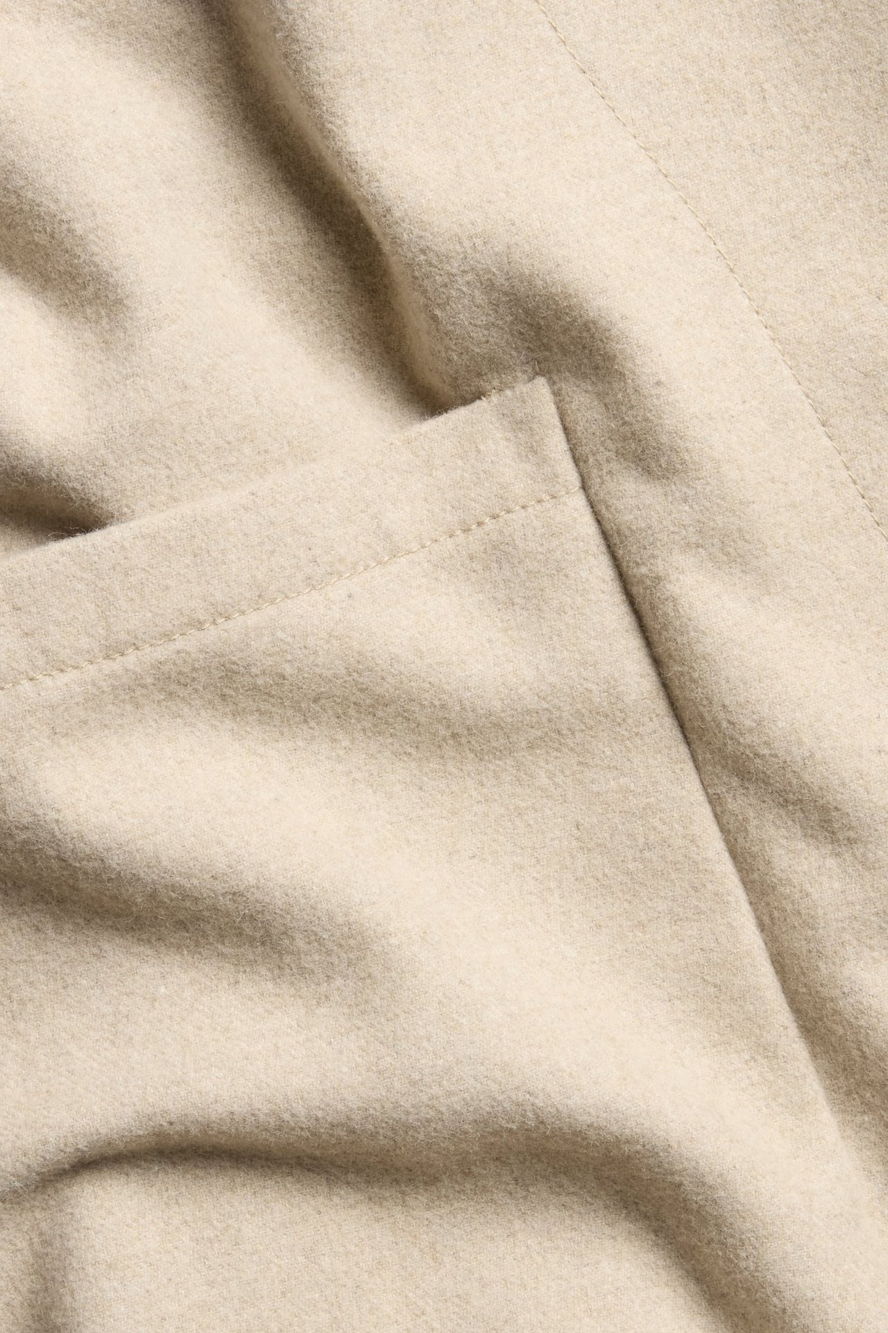 Zbliżenie beżowego melanżowego materiału kurtki z mieszanki wełny z widocznym szwem.