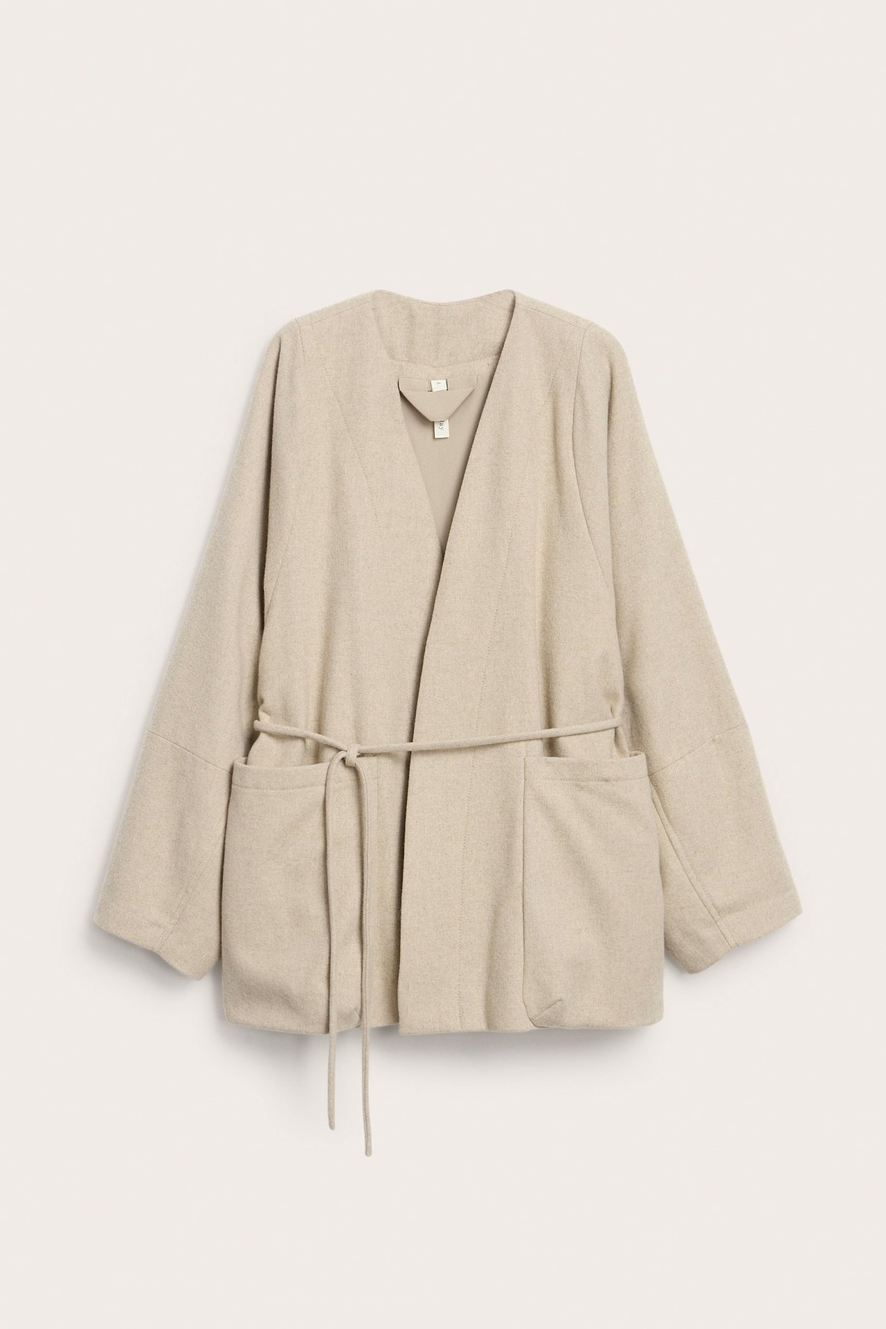 Edestä: beigemelerattu villasekoitepusero, jossa V-pääntie, solmittava vyö ja suuret etutaskut.