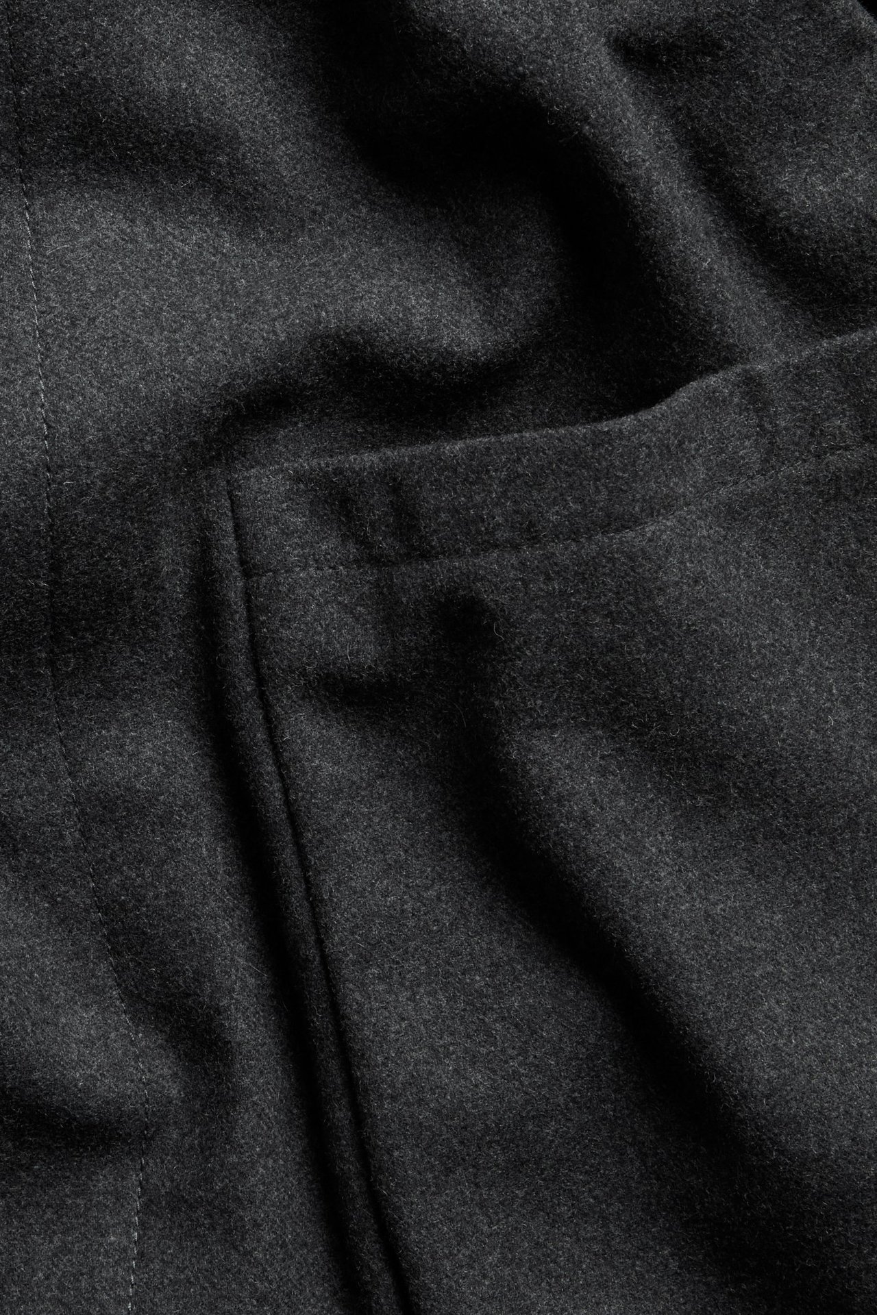 Zbliżenie na ciemnoszary melanżowy materiał kurtki z domieszką wełny, widoczne przeszycia i kieszeń.