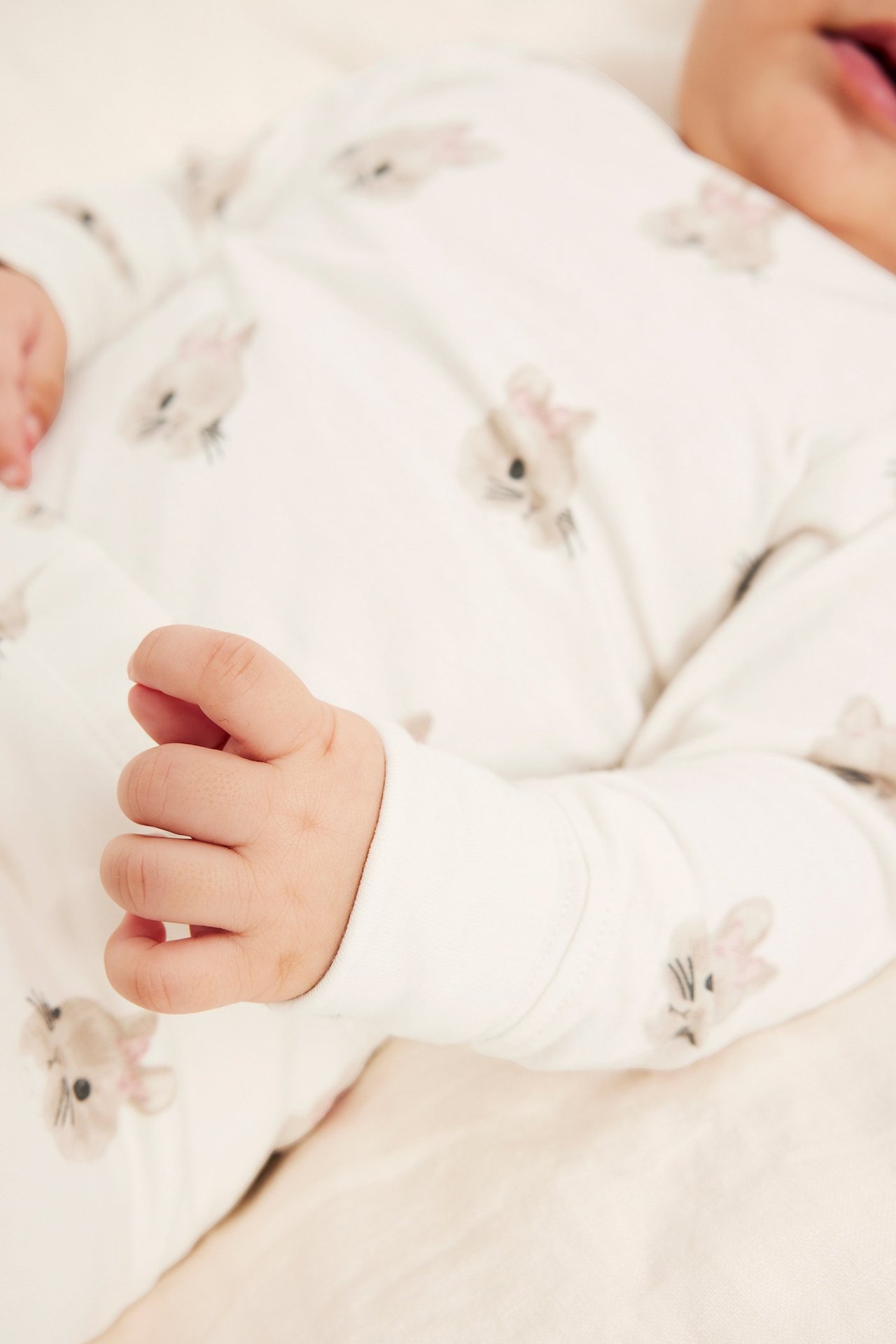 Lähikuva vauvasta, jolla on luonnonvalkoinen kuviollinen pitkähihainen puuvillabody pupuaiheella.