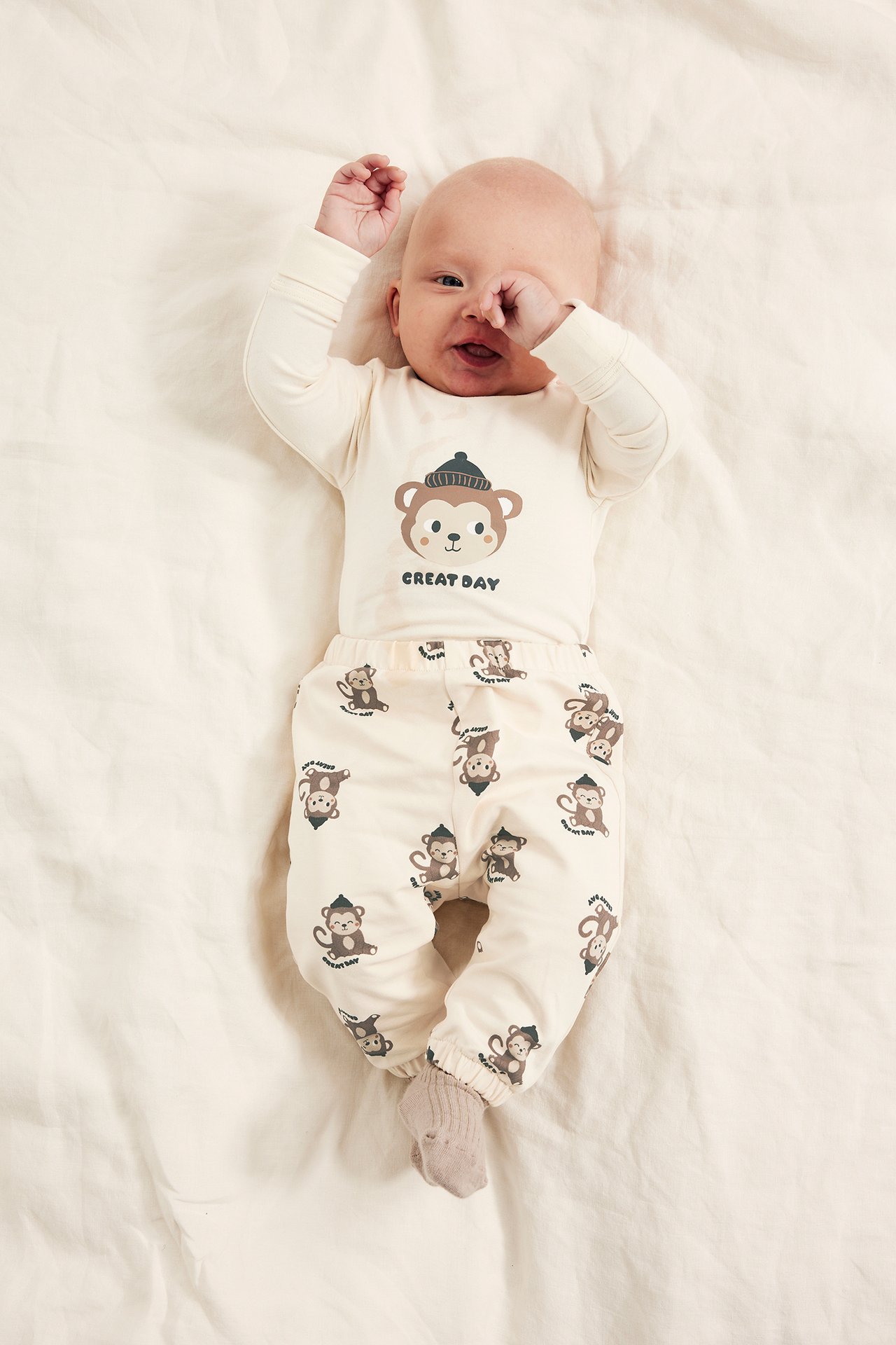 Ylhäältä: vauva vaaleanbeigessä pitkähihaisessa apinaprintti-bodyssa, yhteensopivissa housuissa ja sukissa.