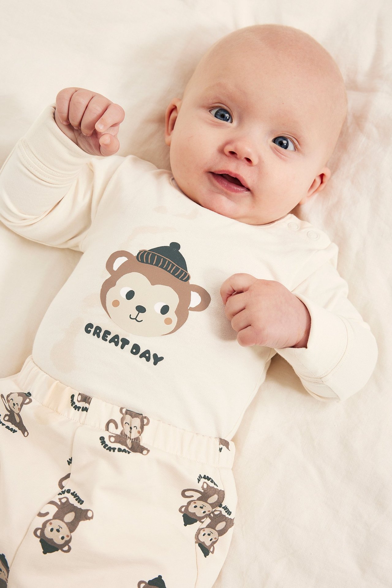 Vauva edestä päin yllään vaalea beige pitkähihainen body apinaprintillä ja yhteensopivat kuvioidut housut.