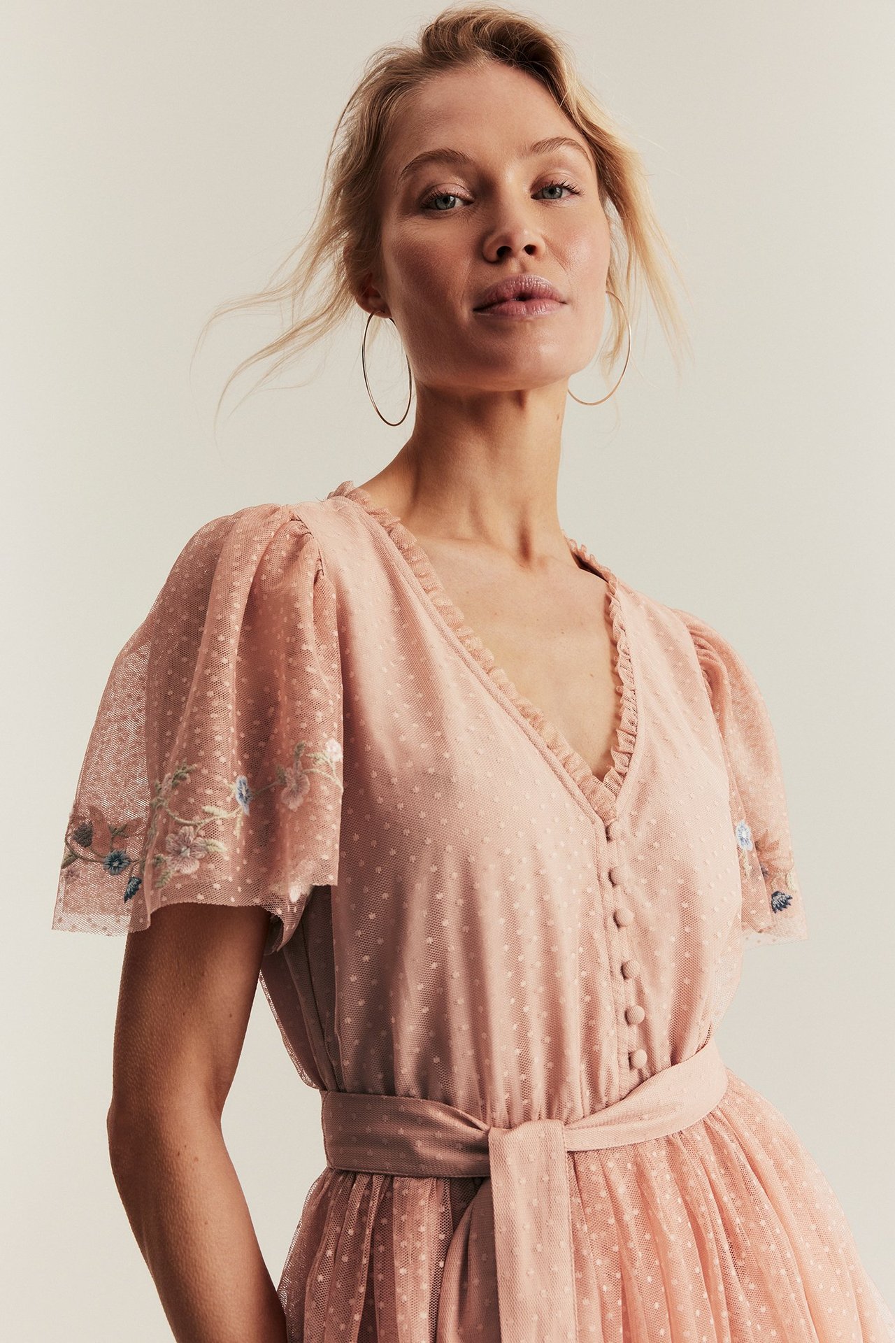 Framsida: Kvinna i rosa prickig meshklänning med broderade ärmar, knappar fram och knutet skärp.