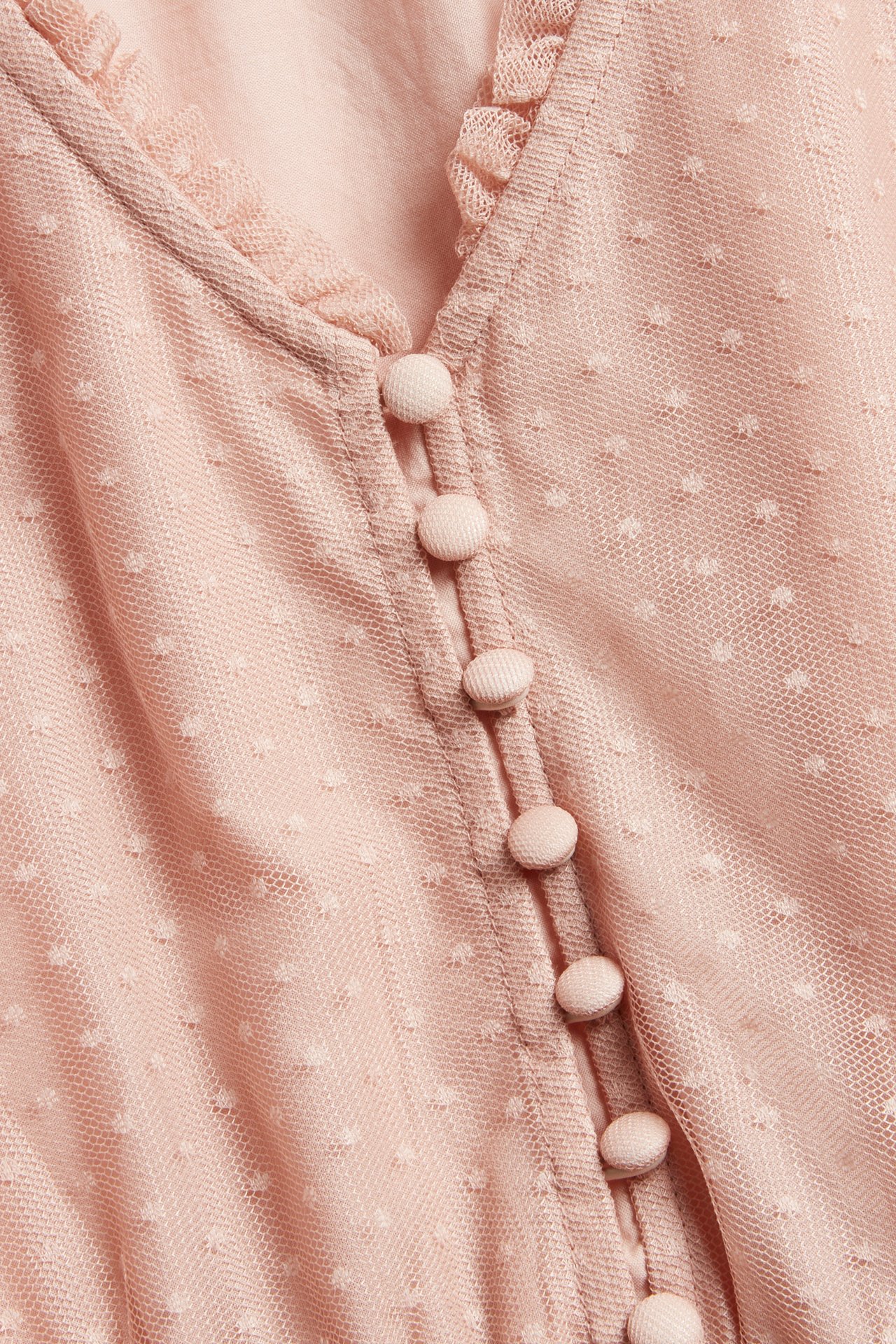 Nærbilde av en rosa prikket meshkjole til dame med V-hals, liten volang og stofftrukne knapper.