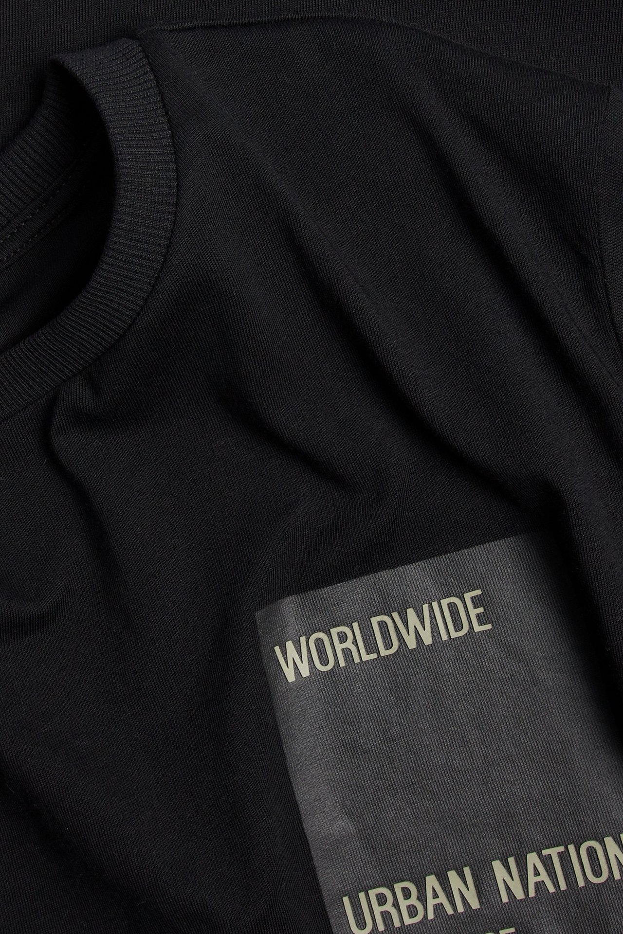 Zbliżenie na czarny bawełniany t-shirt z szarym nadrukiem na piersi 'WORLDWIDE URBAN NATION'.