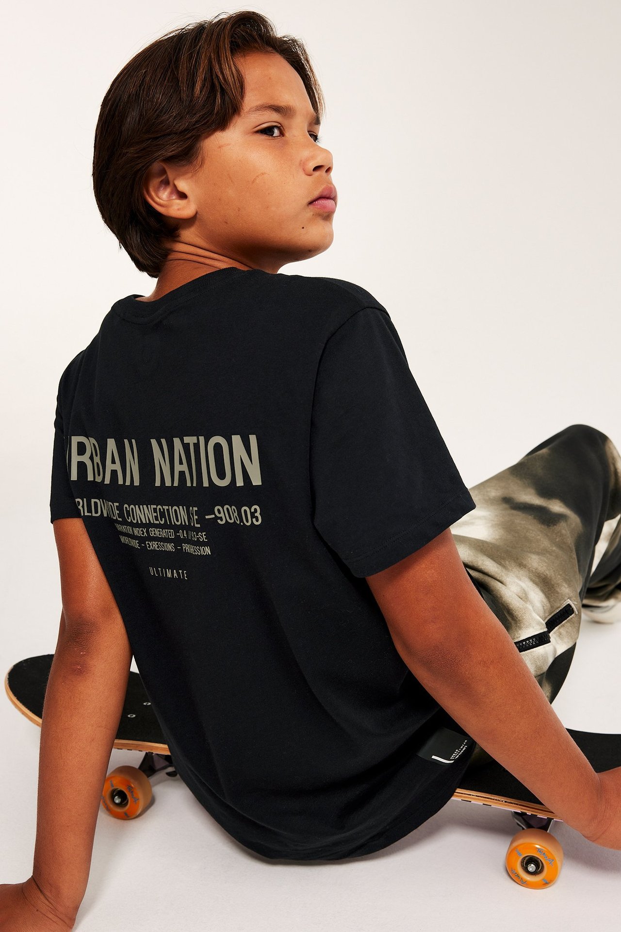 poika mustassa printtivärissä T-paidassa, istuu laudalla, sivuprofiili.