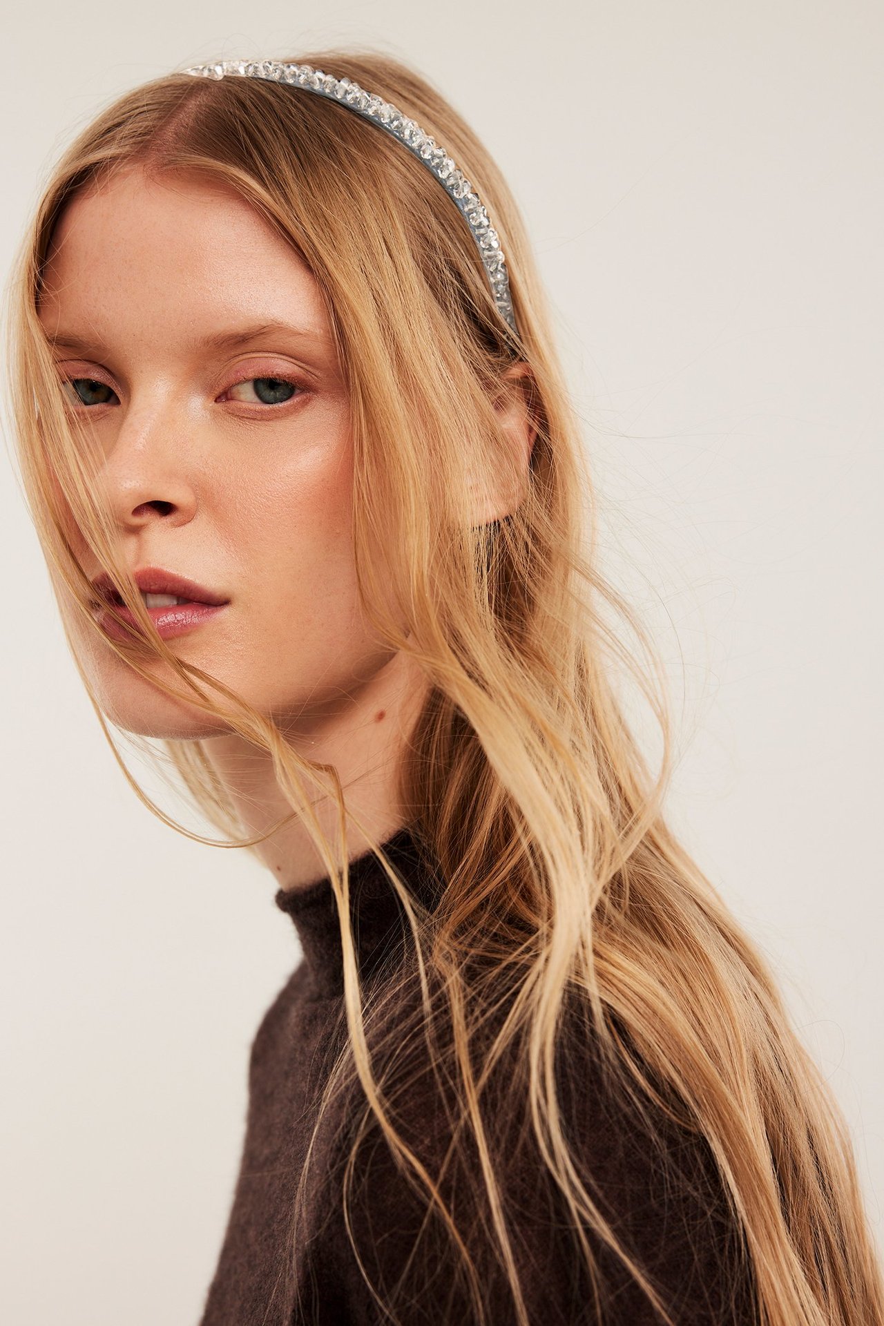 Lähikuva naisesta, jolla on hopeinen strassipanta ja tummanruskea poolokauluspaita.