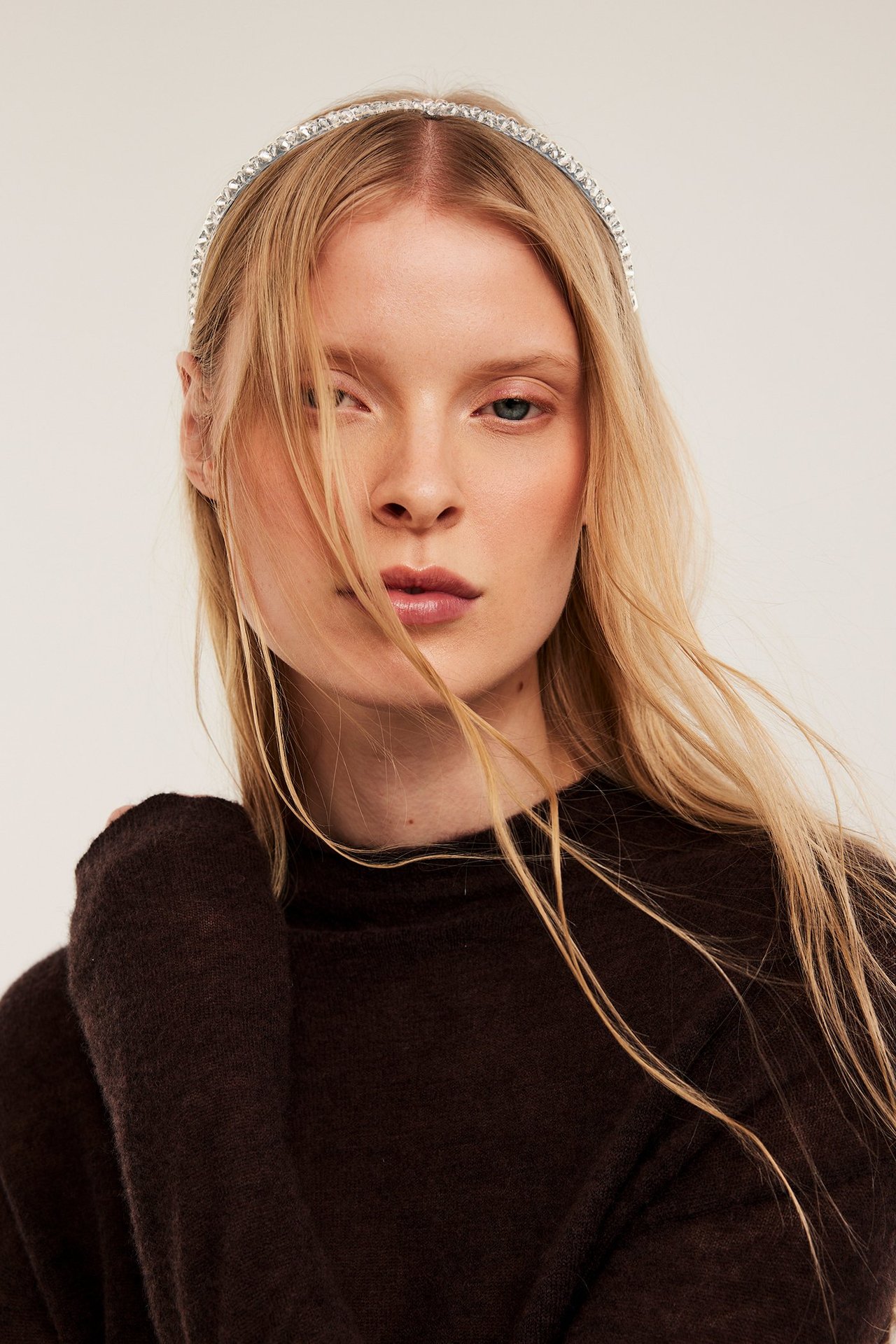 Lähikuva naisesta, jolla on hopeanvärinen strassipanta ja tummanruskea neule.