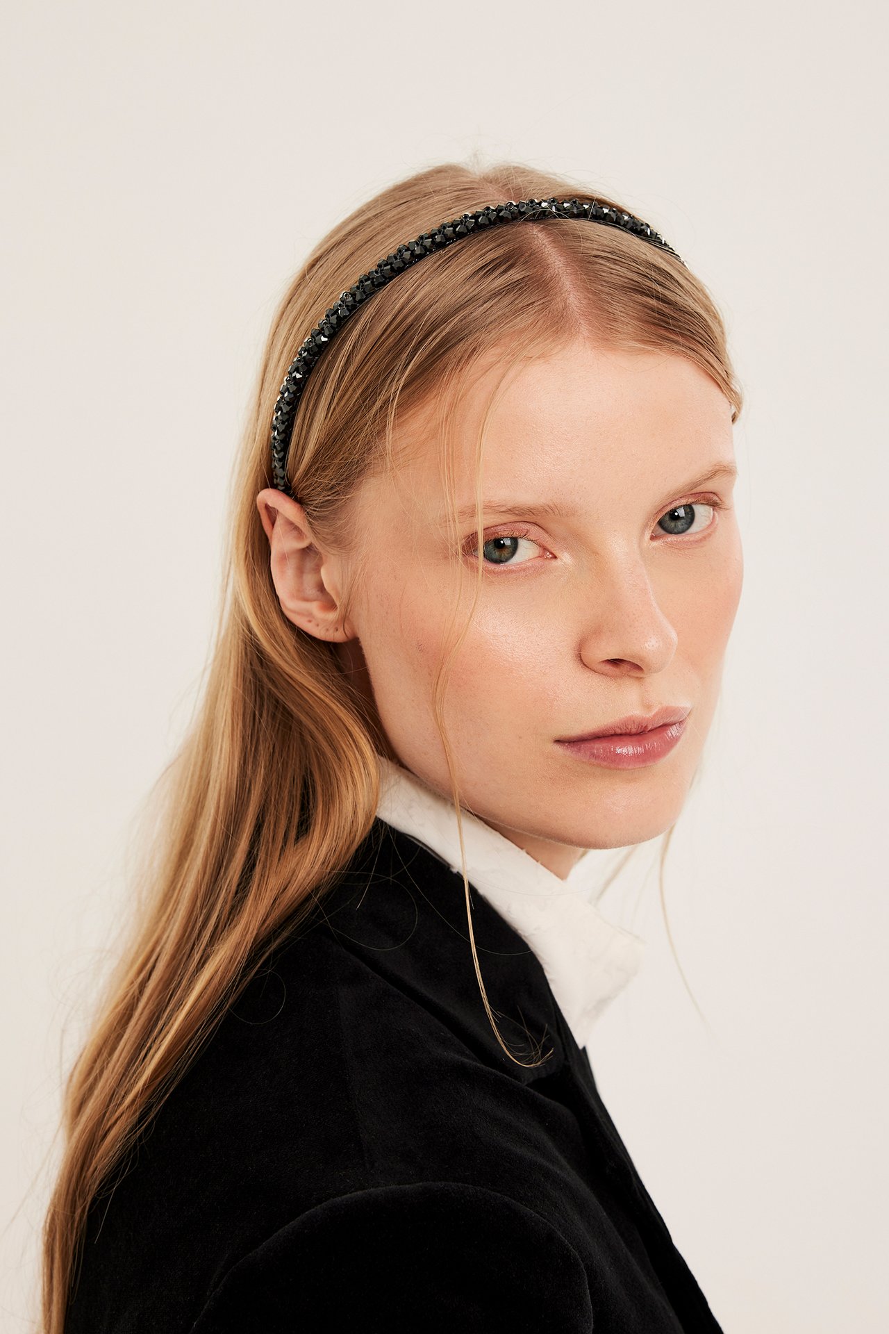 Lähikuva naisesta, jolla on musta strassipanta, valkoinen paita ja musta takki.