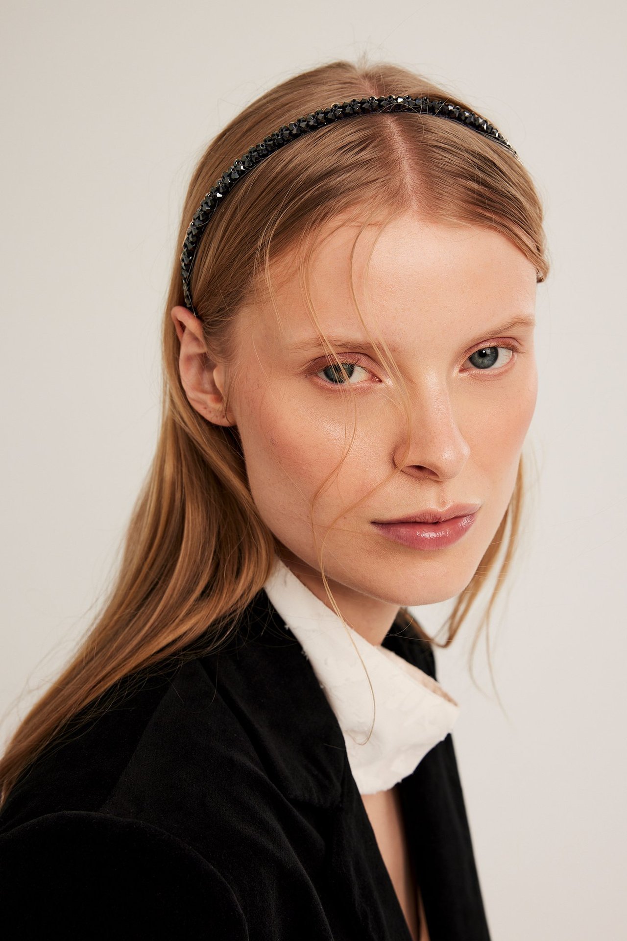 Edestä, nainen mustassa strassipannassa, mustassa takissa valkoisen paidan päällä.