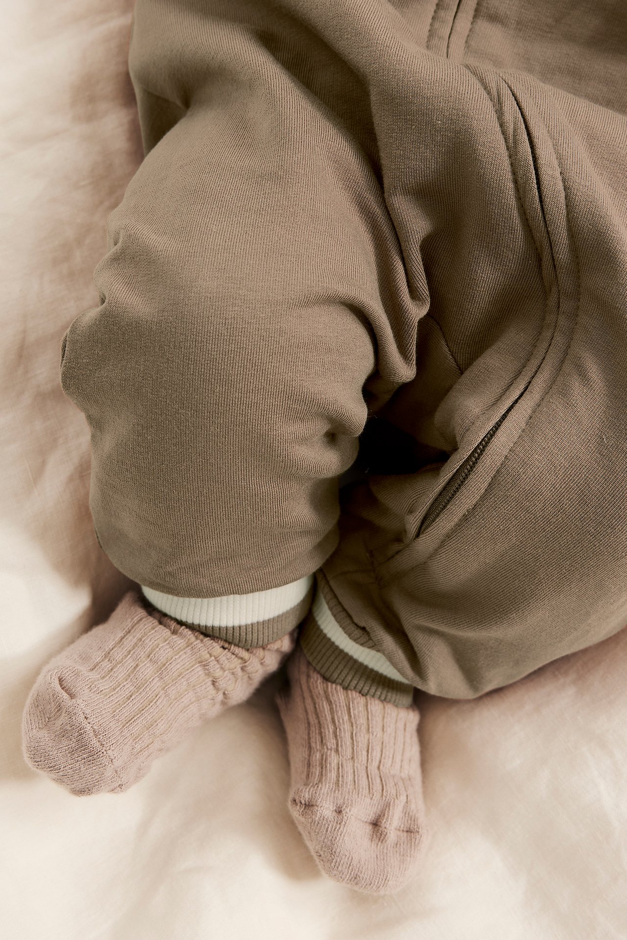 Närbild på baby i brun bomulls-sweatshirtoverall med randiga ribbmuddar och rosa ribbade strumpor.