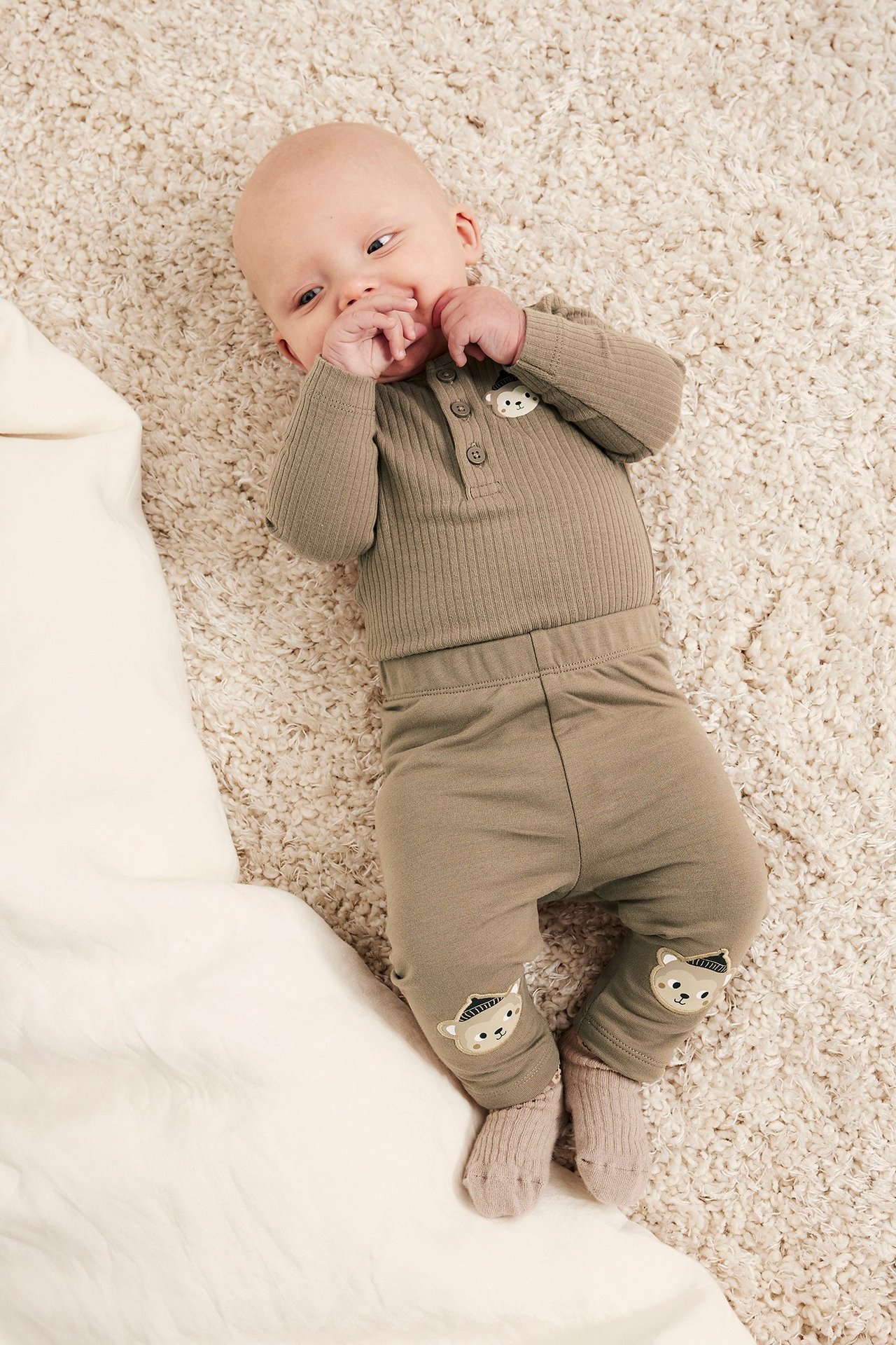 Ylhäältä kuvattu vauva ruskeissa lämpöleggingseissä eläinapplikaatioilla, ribatussa bodyssä ja vaaleanruskeissa sukissa.