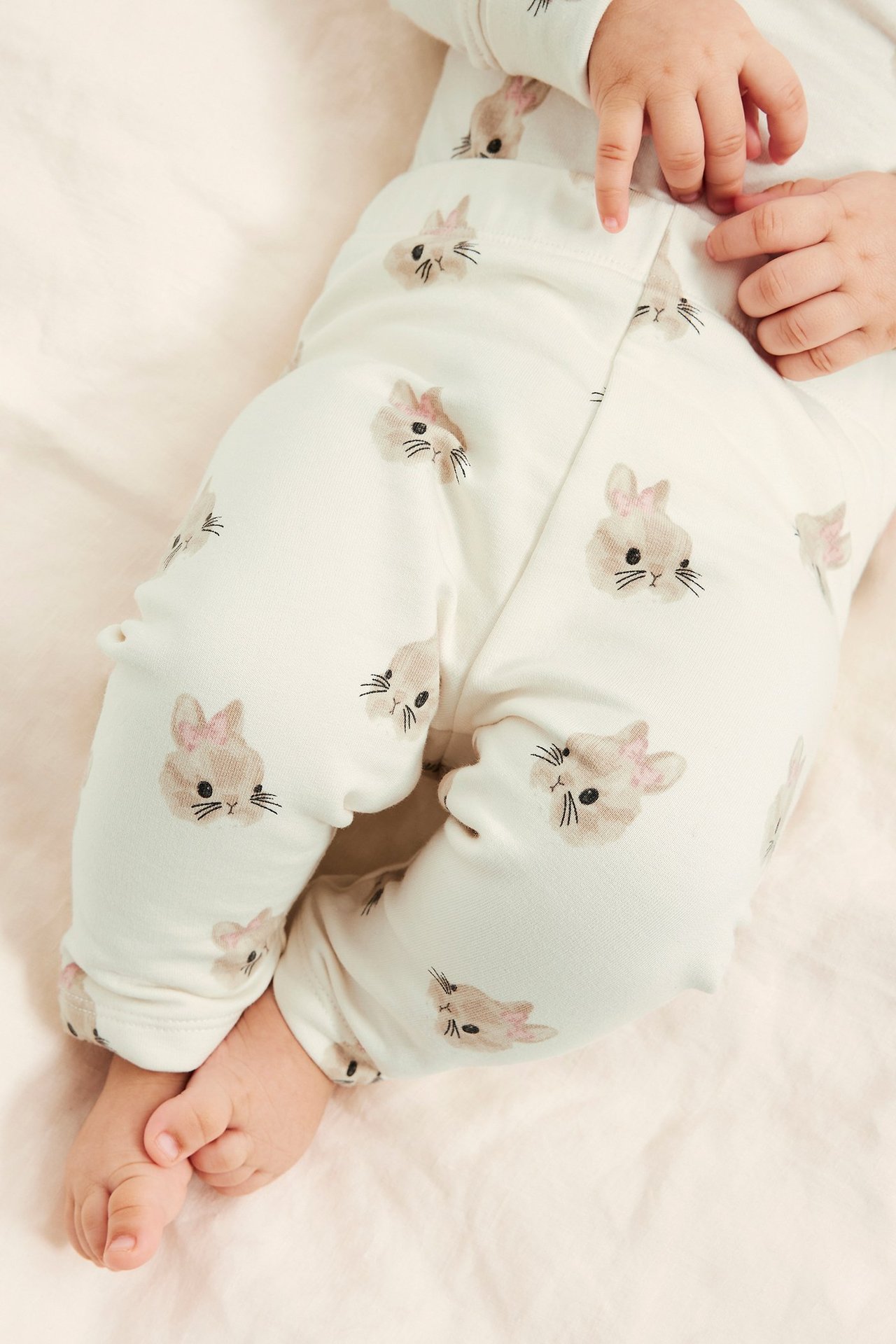 Lähikuva vauvasta offwhite-puuvillaleggingsissä, joissa on kauttaaltaan kanikuviointi.