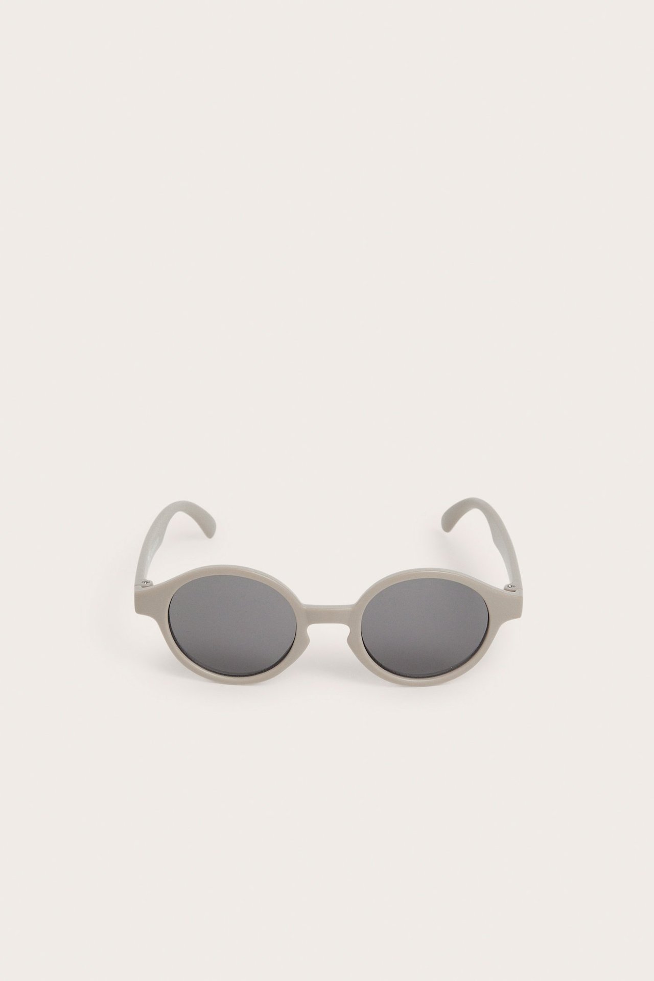 Widok z przodu beżowych owalnych okularów przeciwsłonecznych dla niemowląt z ciemnymi szkłami.