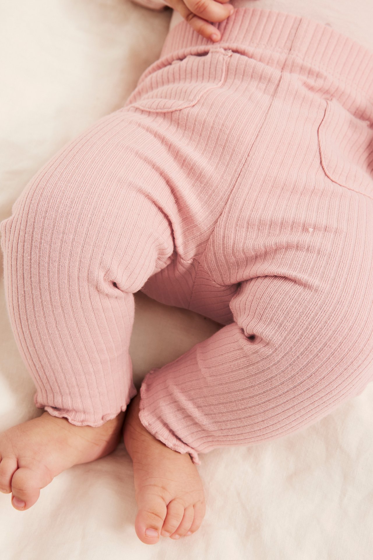 Närbild på en baby som bär rosa ribbade leggings i bomull med resår i midjan och volangmuddar.