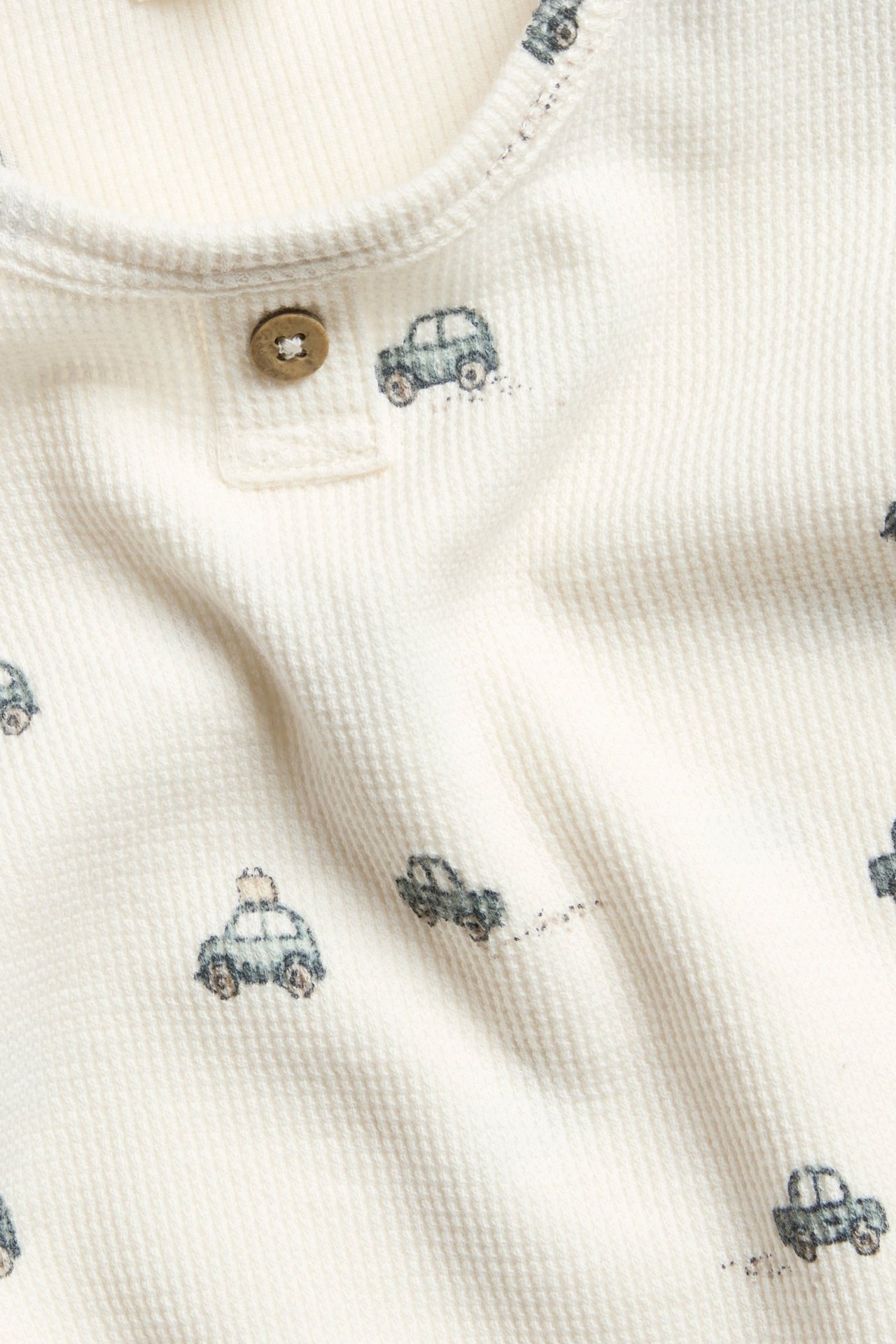 Valkoinen pitkähihaisessa bodyn vaahtokarkkuneuloksessa, autokuvio, nappi edessä ja printtiripissä.