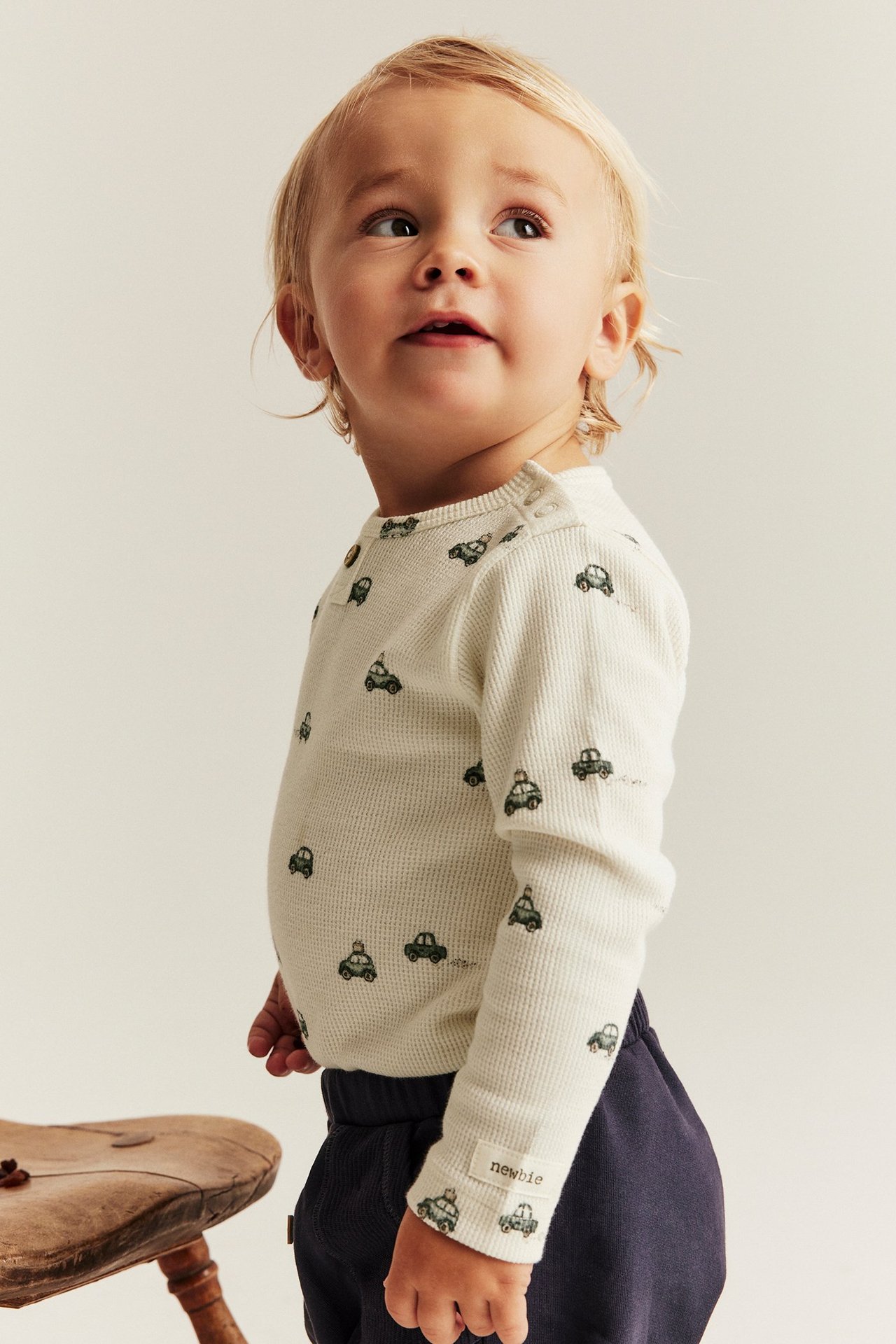 Sidovy av baby i offwhite våffelstickad body med grönt bilmönster och mörkblå byxor.