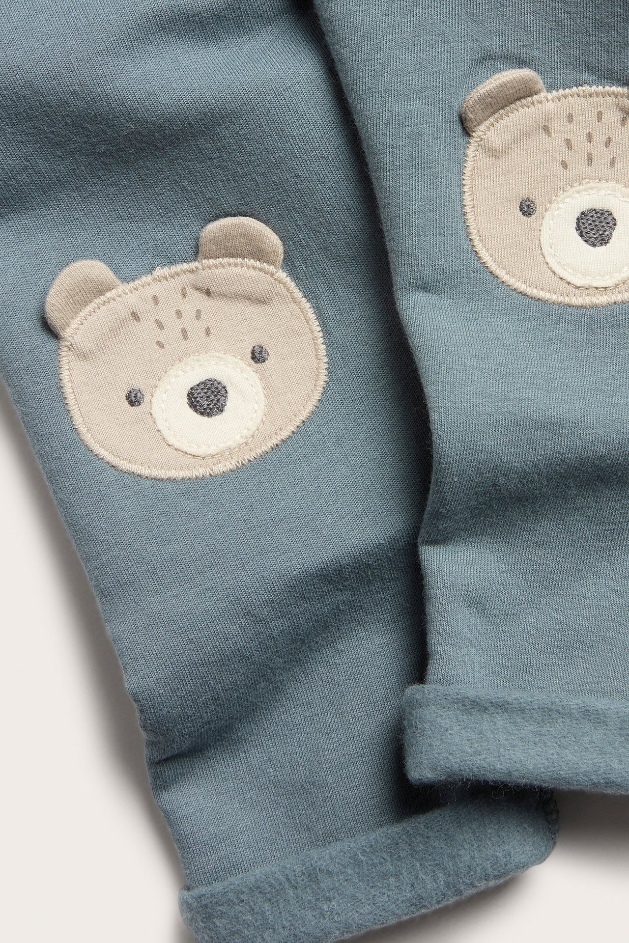 Siniset fleecelegginsit, karhuapplikaatio, polvipalat, koristeelliset edessä olevat napit ja kääntyvät lahkeet.