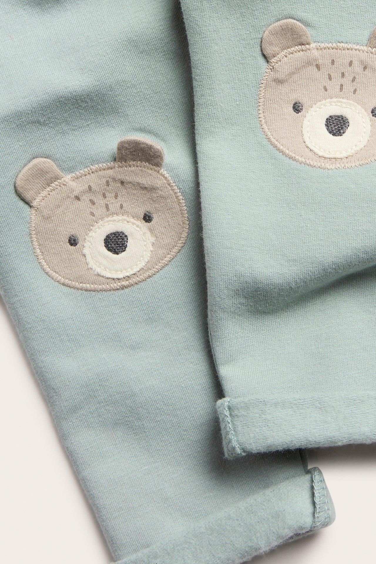 Nærbilde av lys grønne barneleggings med børstet innside og beige bjørneansikt-applikasjoner.