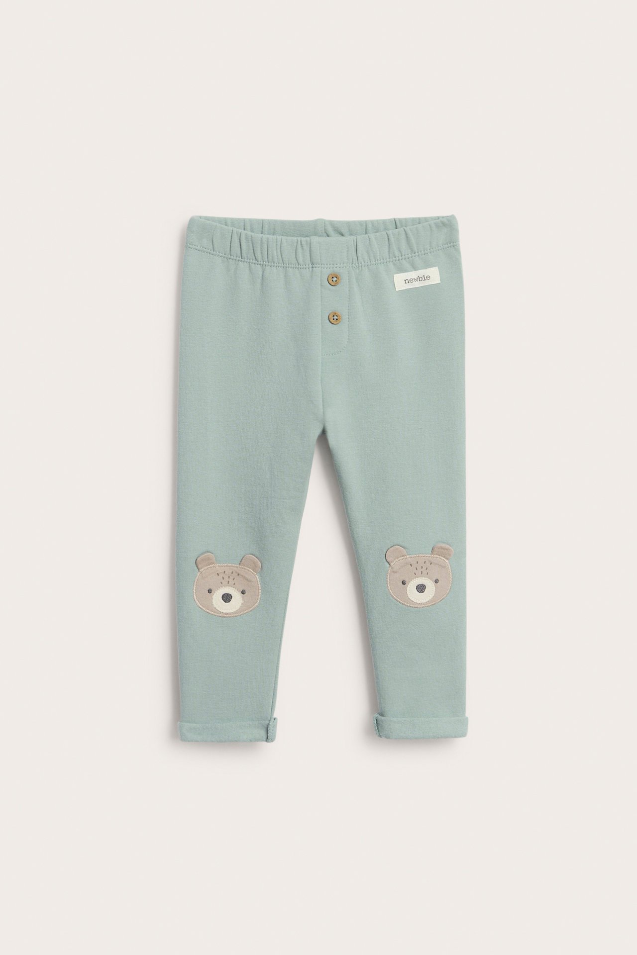 Frontvisning av babyens lysegrønne børstede bomullsleggings med bjørneapplikasjoner på knærne og dekorative knapper.