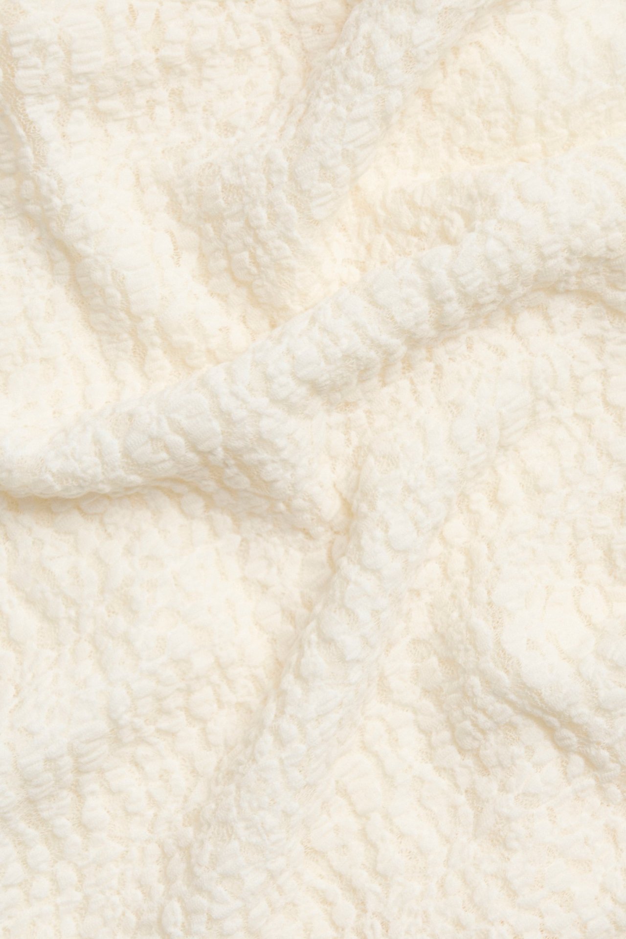 Zbliżenie na ecru koronkowy materiał na top, z delikatnymi detalami babylock.