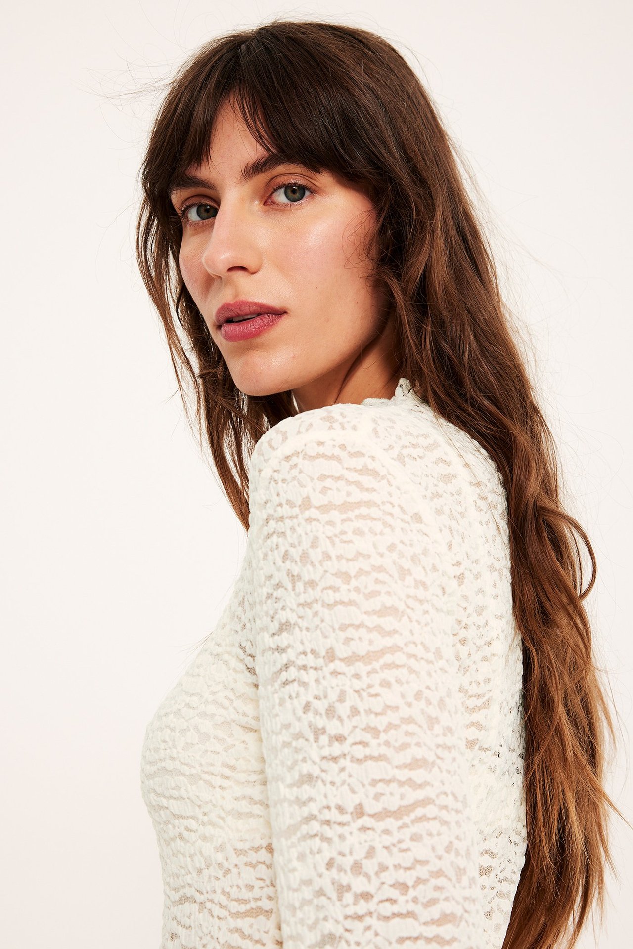 Lähikuva, sivukuva naisesta yllään luonnonvalkoinen pitkähihainen pitsitoppi babylock-yksityiskohdilla.