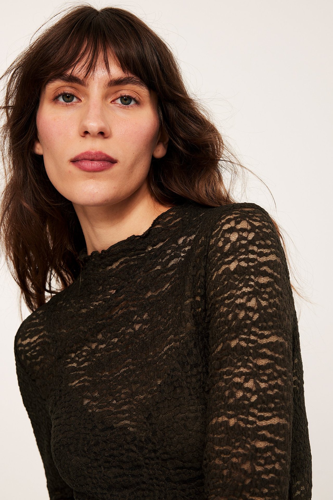 Zbliżenie na kobietę w ciemnobrązowym, długim koronkowym topie z detalami babylock.